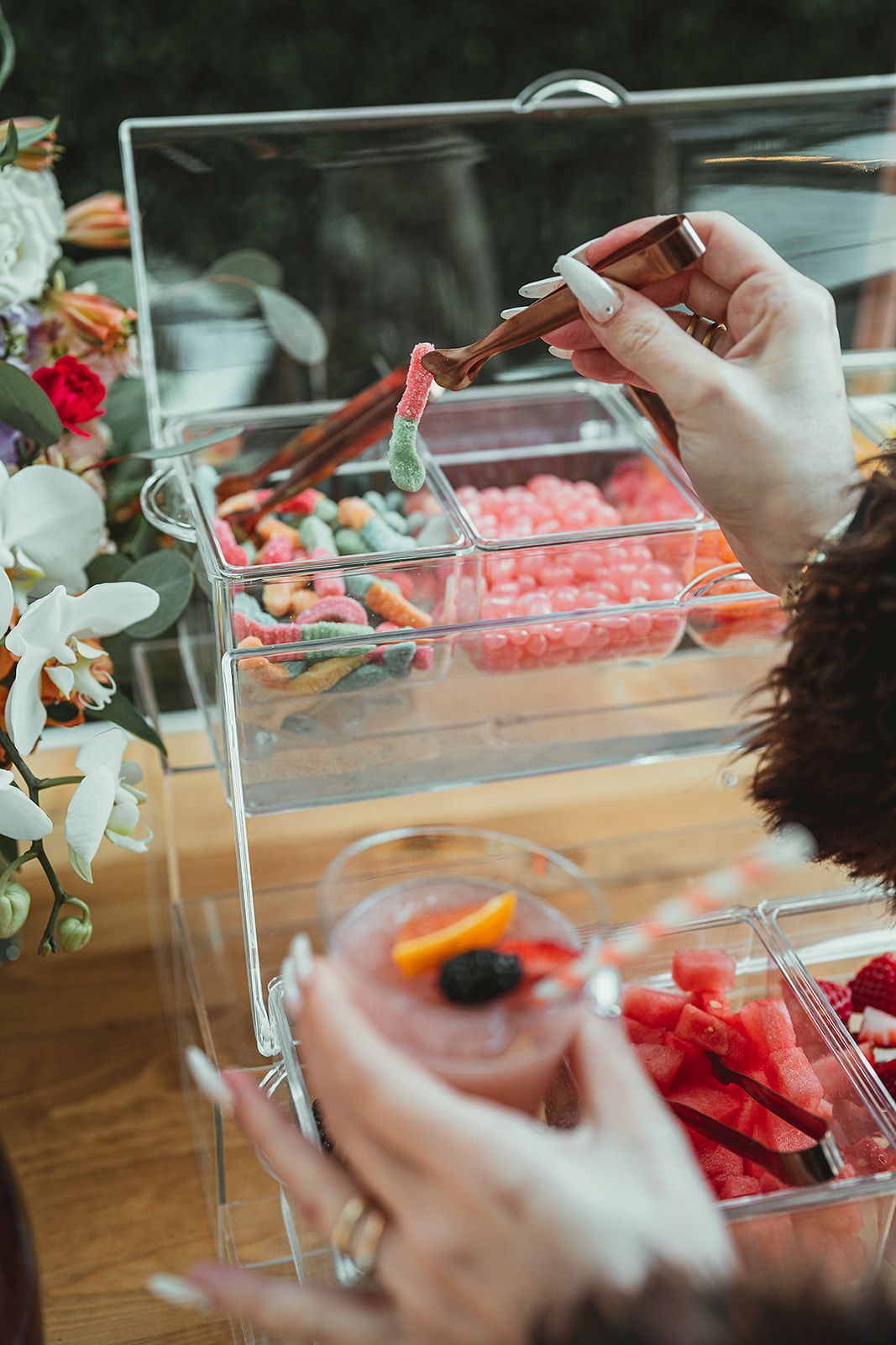 A woman is holding a glass of watermelon and a container of candy.