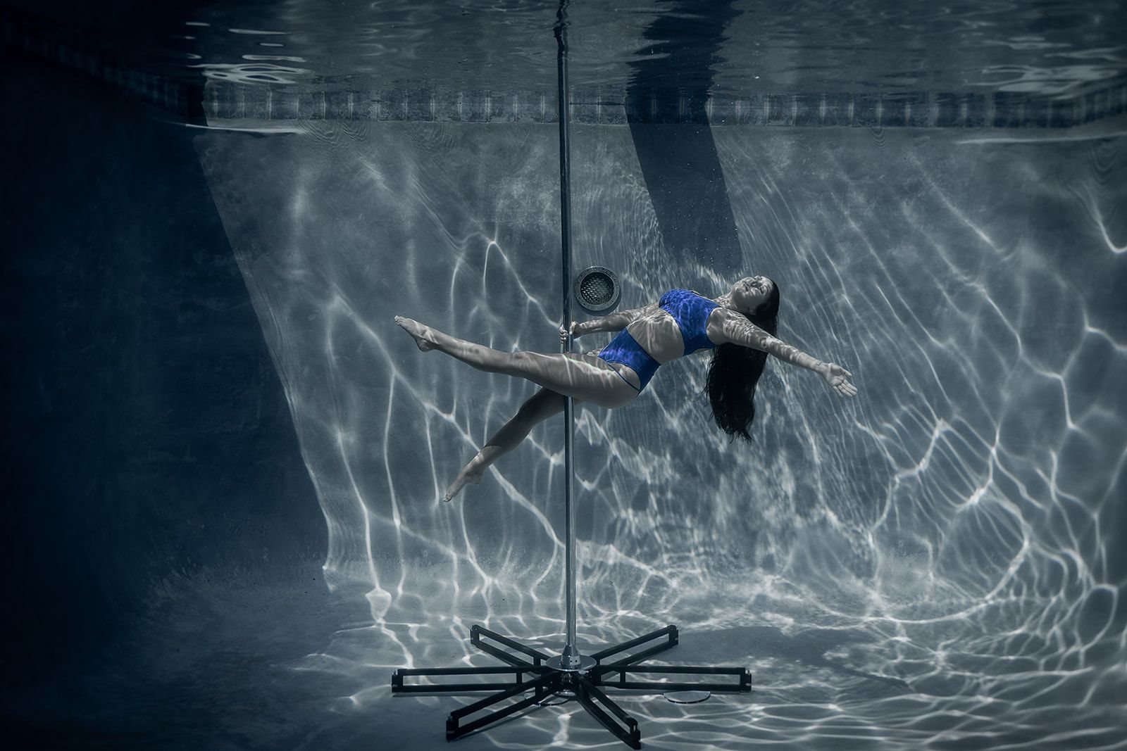 A woman is floating underwater on a pole in a swimming pool.