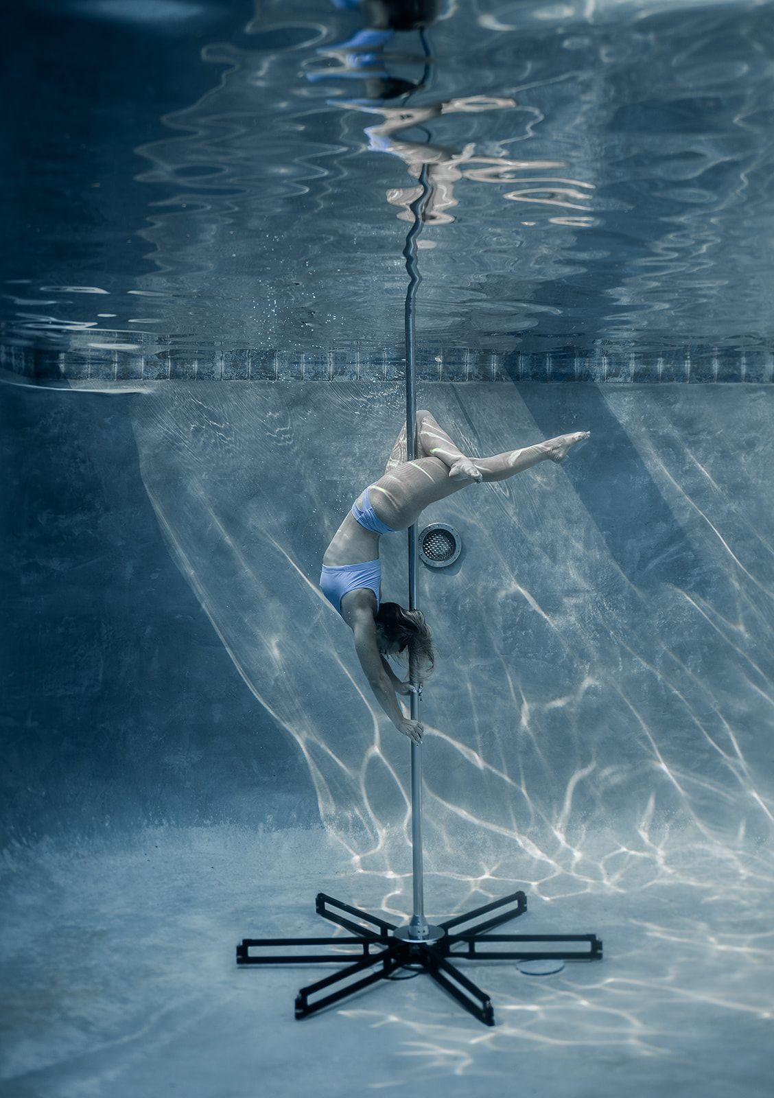 A woman is doing aerial acrobatics underwater in a swimming pool.