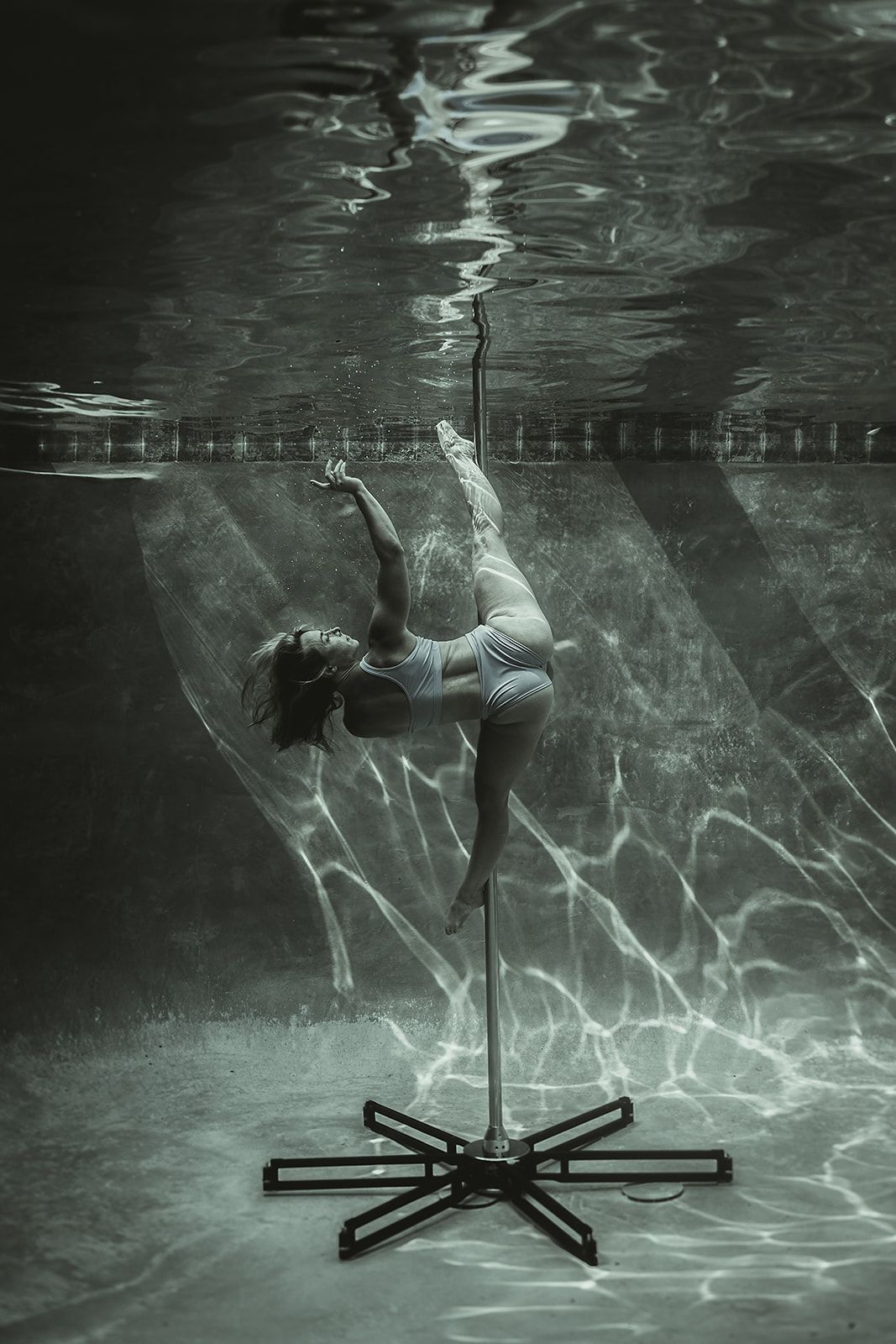 A woman is standing on a pole underwater in a pool.