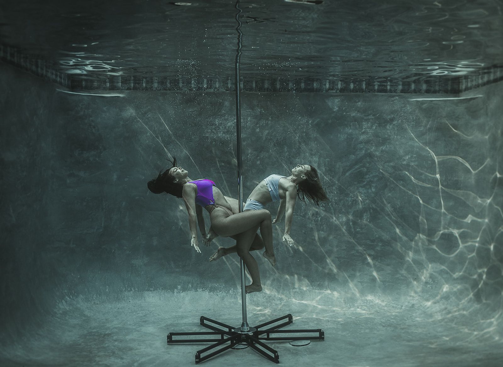 Two women are dancing on poles underwater in a pool.