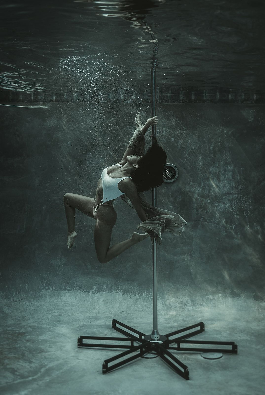 A woman is dancing on a pole underwater in a pool.