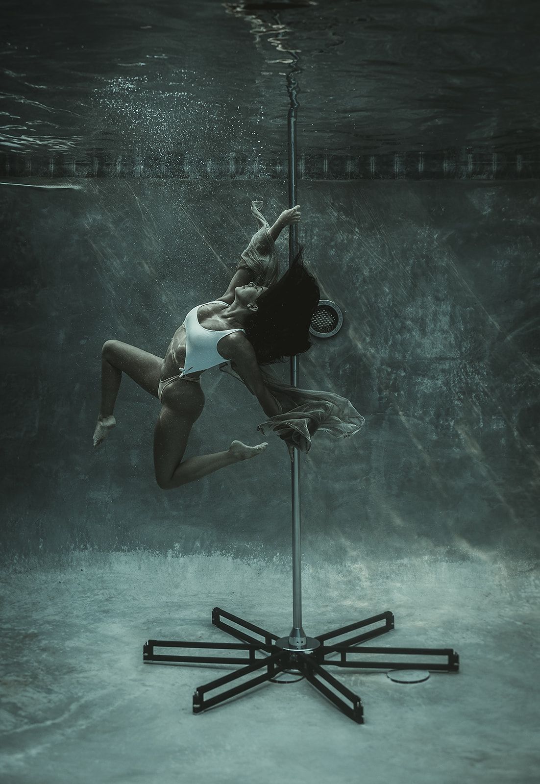 A woman is dancing on a pole underwater in a pool.