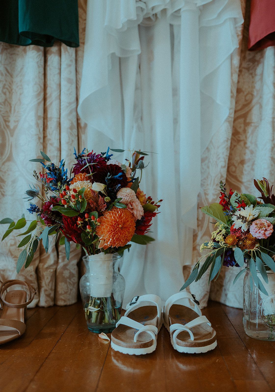A bouquet of flowers and a pair of shoes are on the floor in front of a wedding dress.