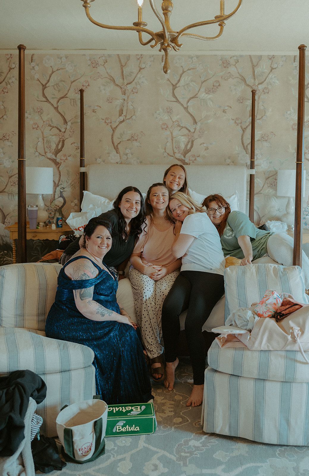 A group of women are sitting on a couch in a bedroom.