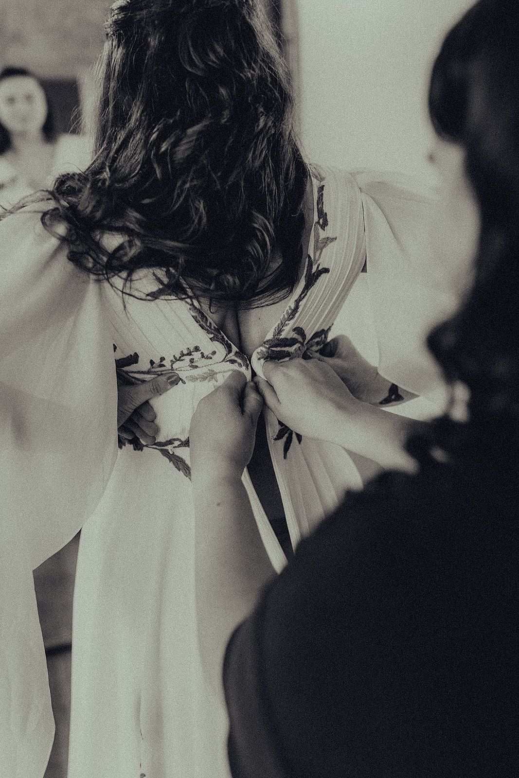 A woman is tying a woman's wedding dress in a black and white photo.
