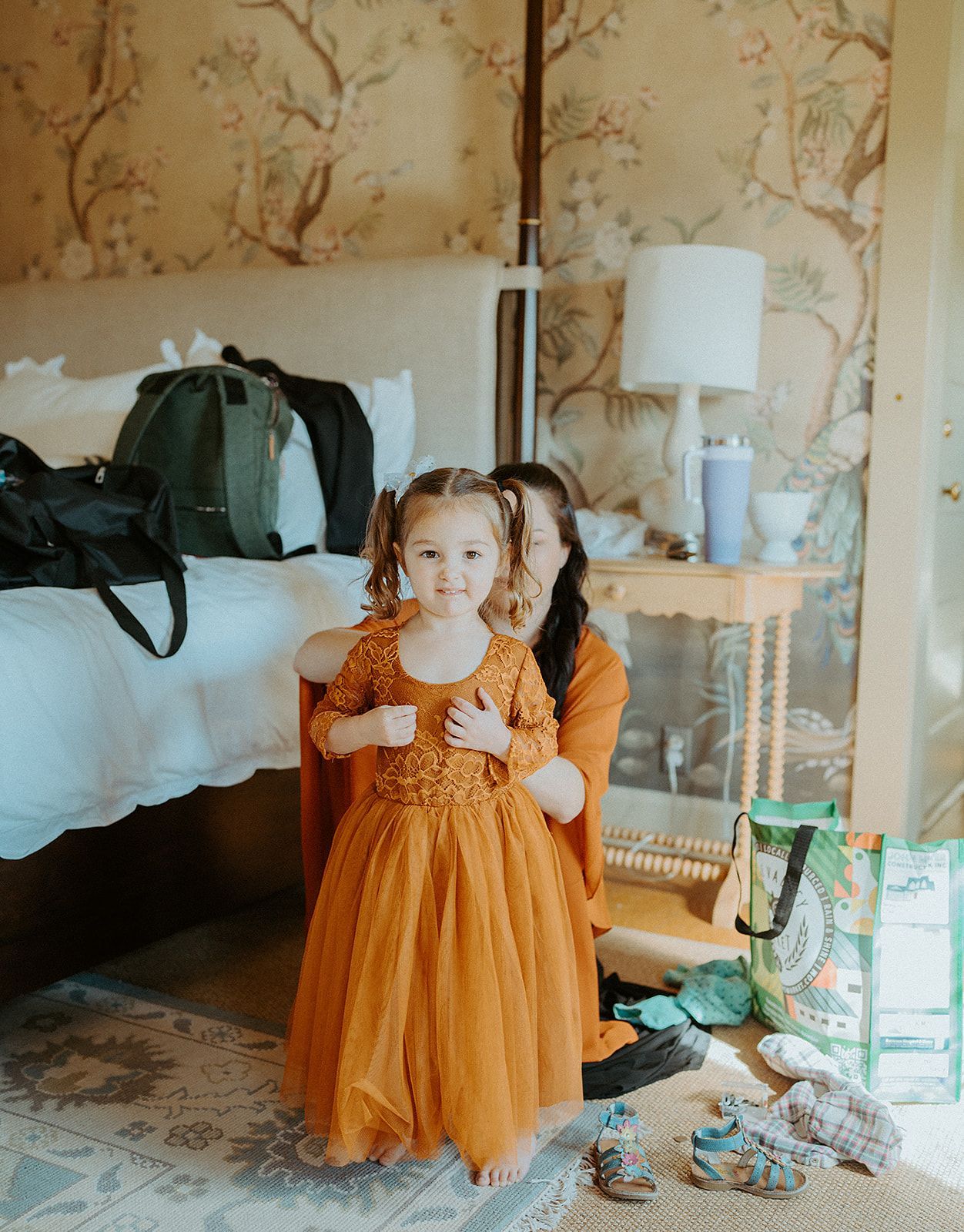 A woman is holding a little girl in an orange dress in a bedroom.