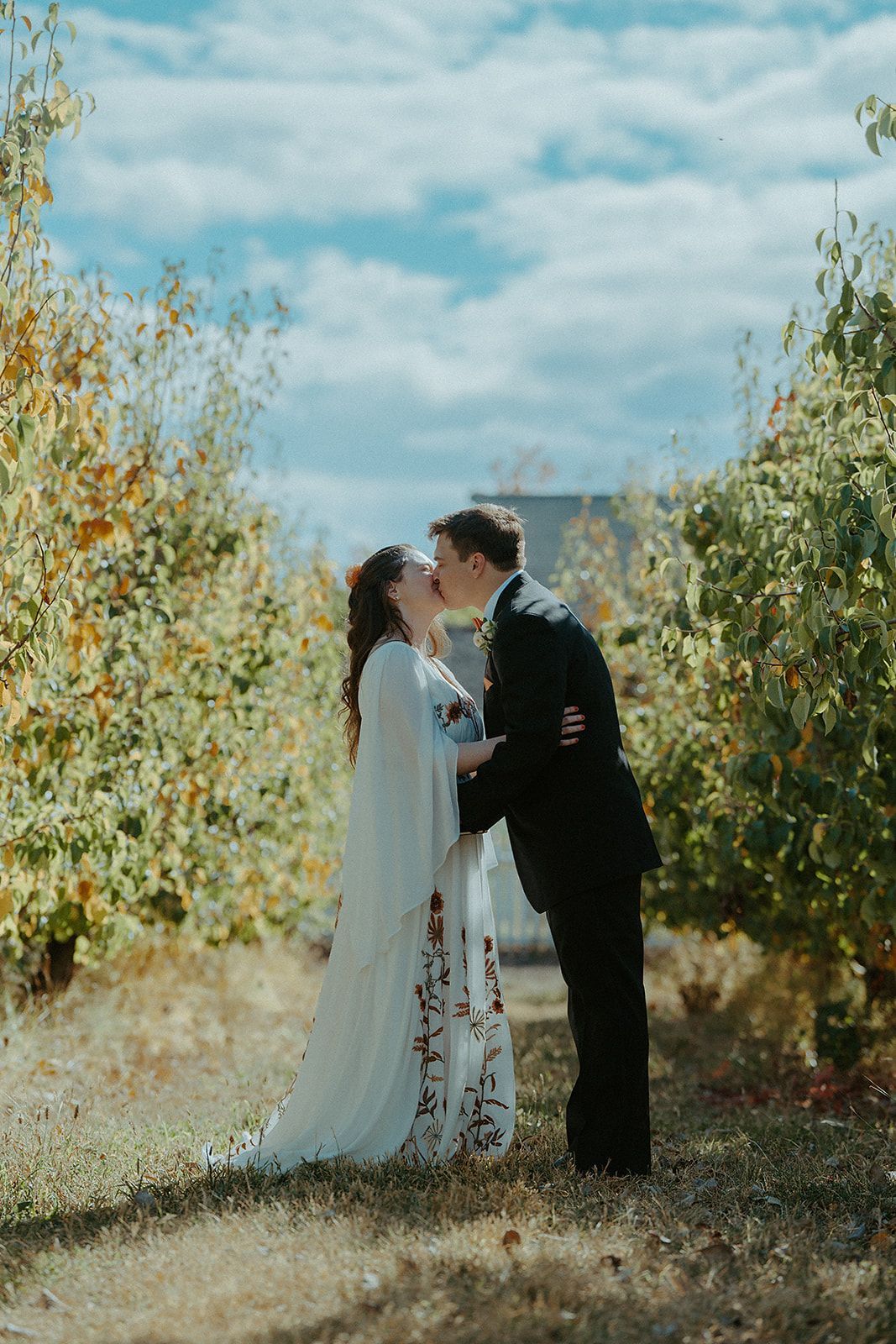 A bride and groom are kissing in a field surrounded by trees.