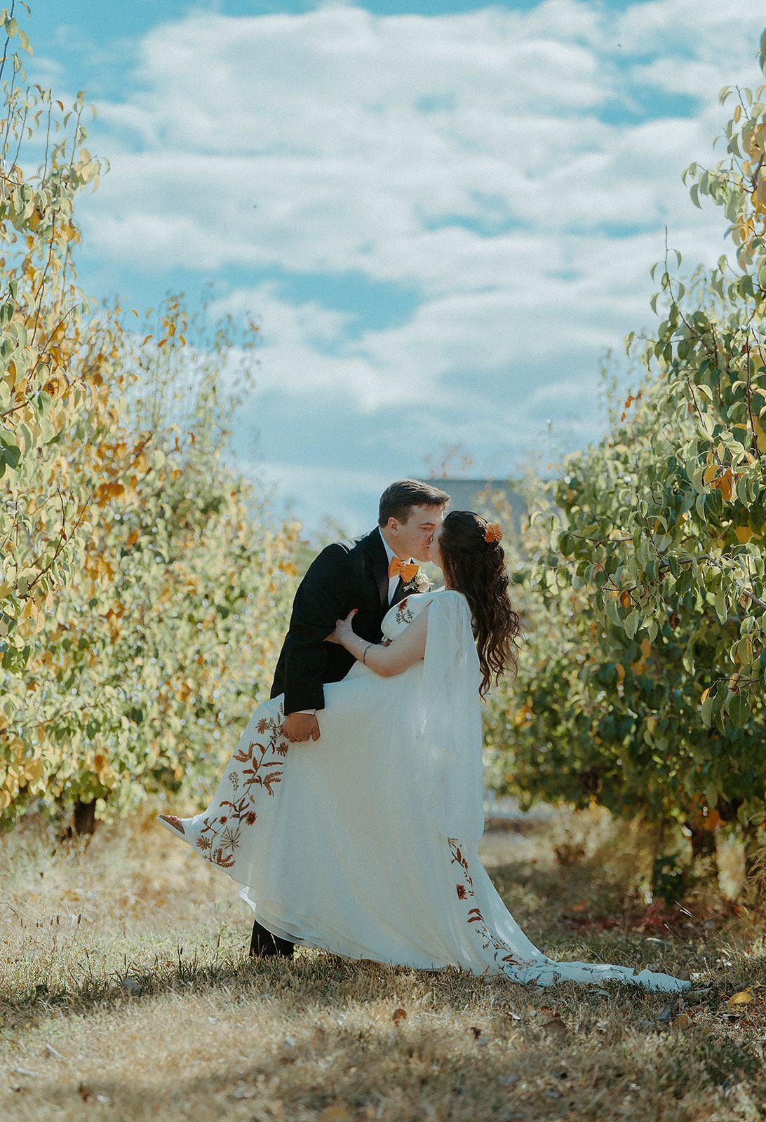 A bride and groom are kissing in an orchard.