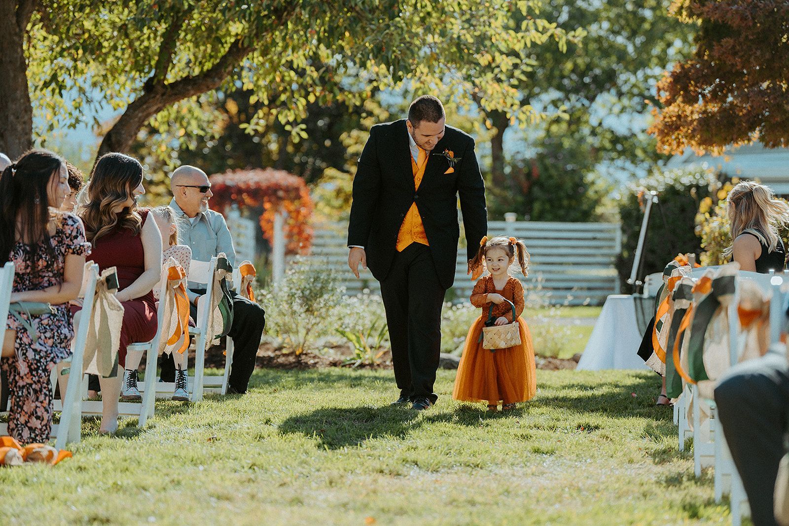 A groomsman and a flower girl walk down the aisle at a wedding.