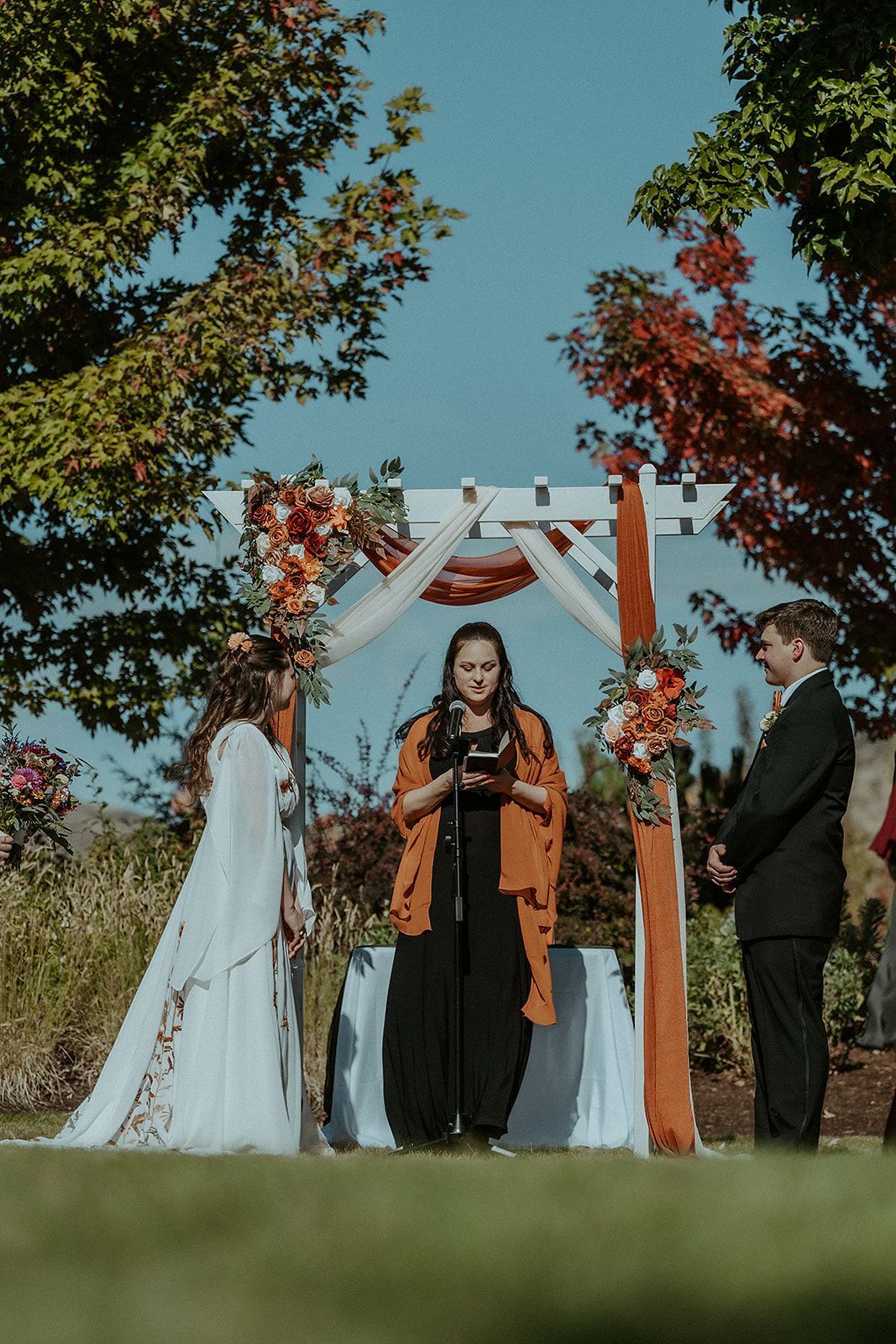 A bride and groom are getting married under a wooden arch.