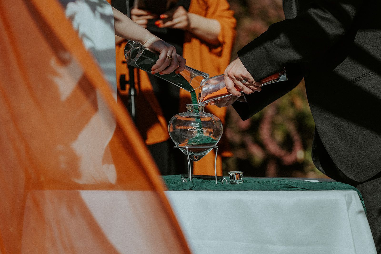 A bride and groom are pouring liquid into a glass during their wedding ceremony.