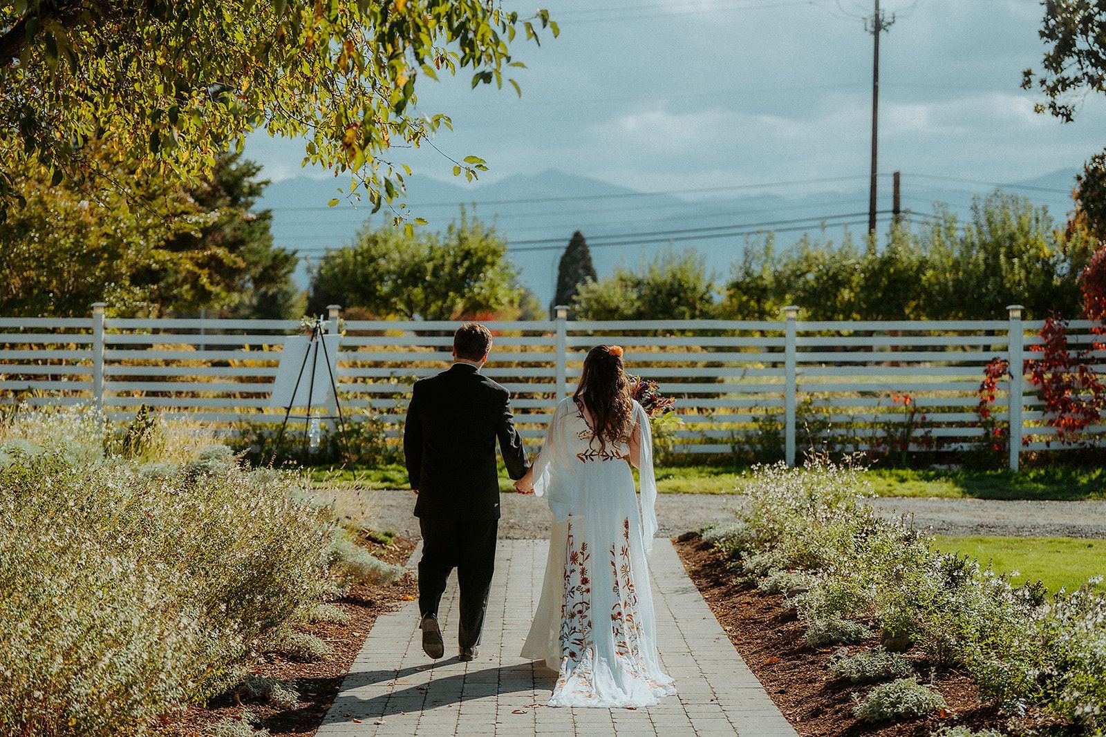 A bride and groom are walking down a path holding hands.