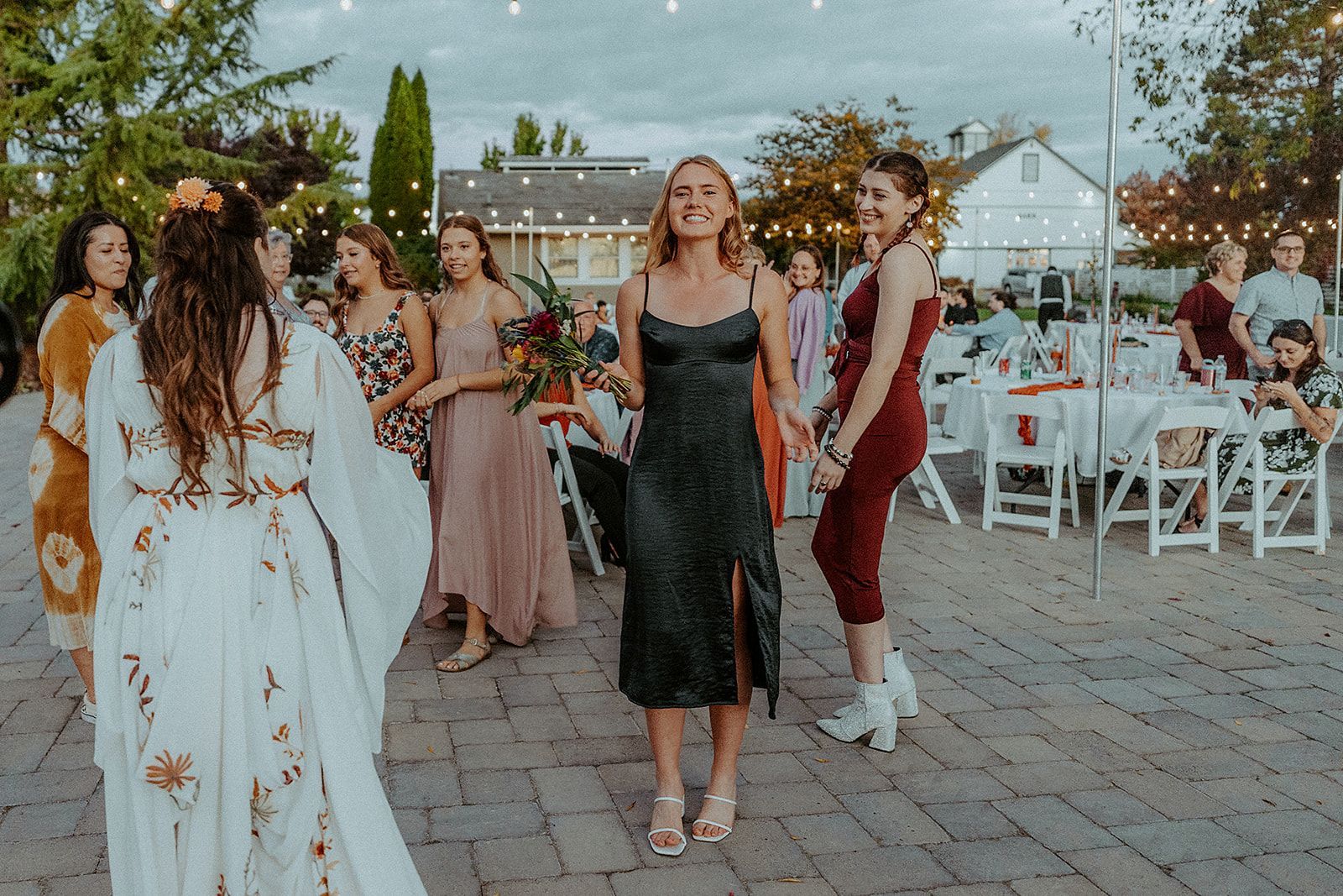 A group of women are standing on a brick sidewalk at a wedding reception.