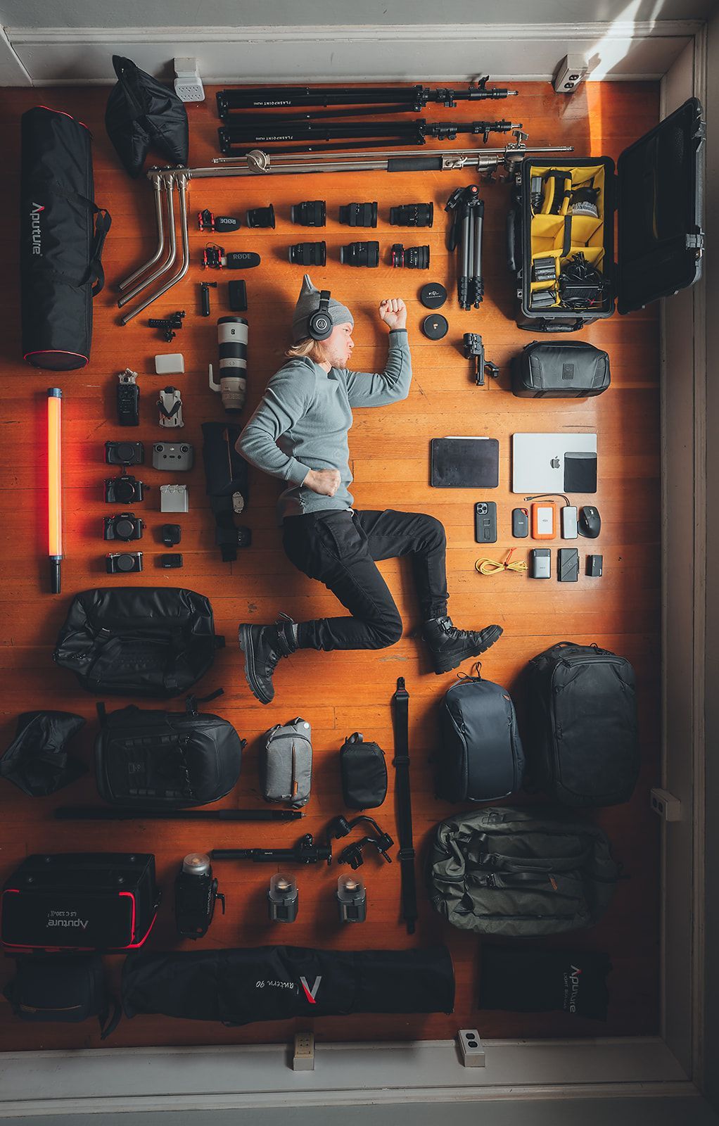 A man is laying on a wooden floor surrounded by camera equipment.