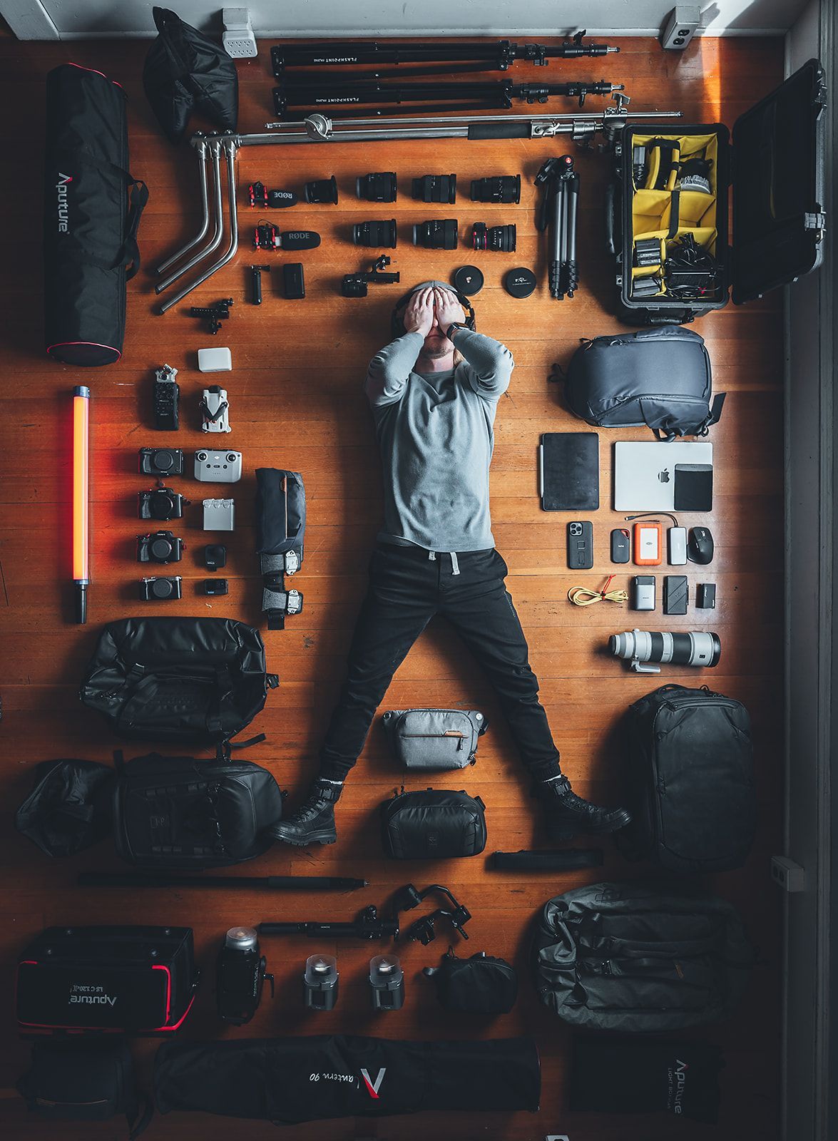 A man is laying on a wooden floor surrounded by camera equipment.