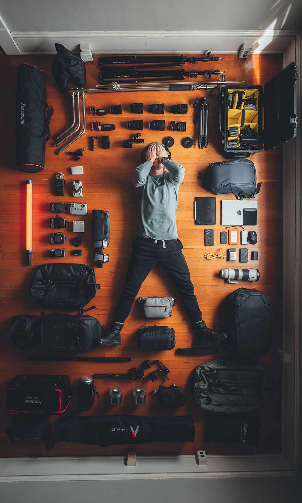 A man is laying on a wooden floor surrounded by camera equipment.