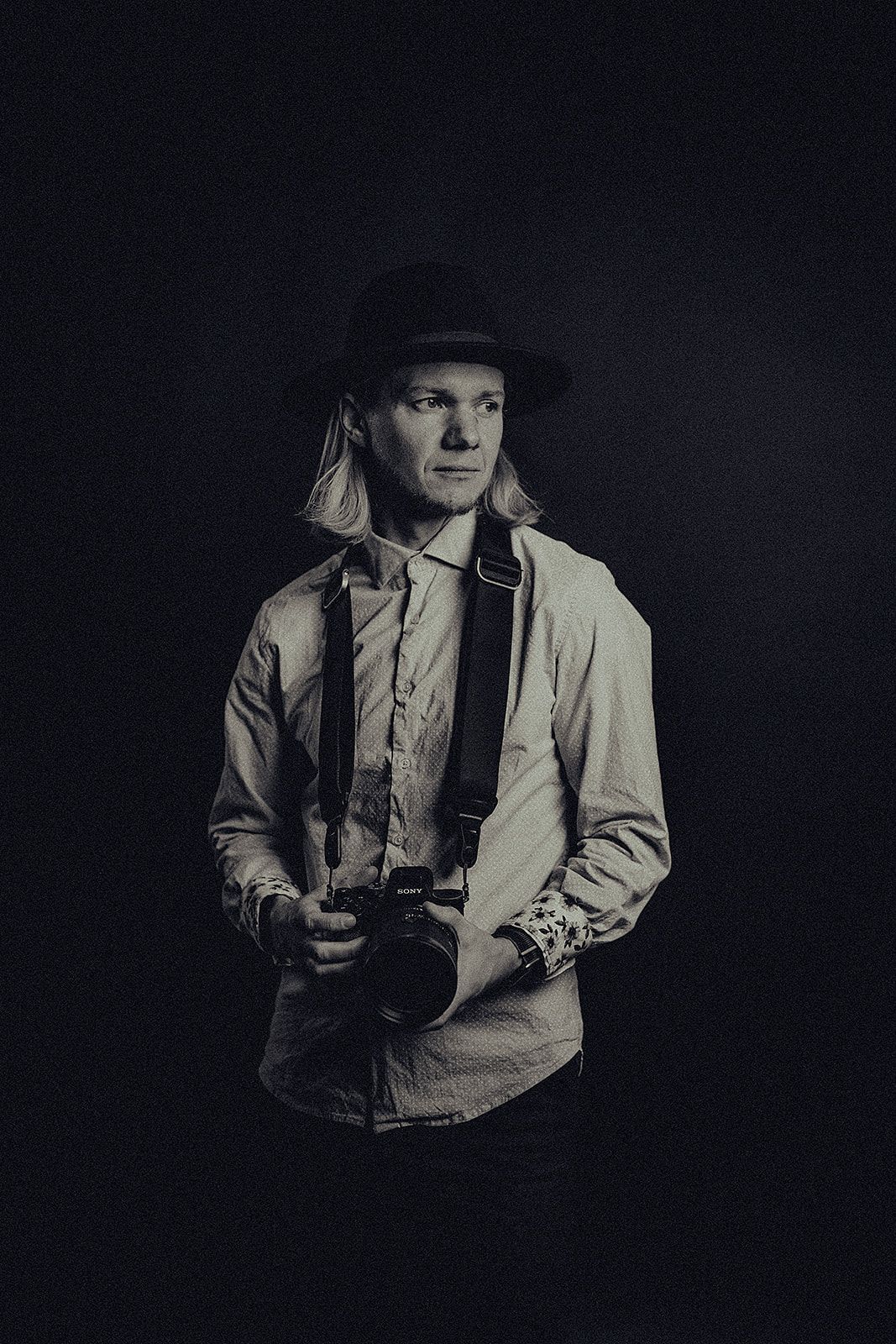 A man in a hat is holding a camera in a black and white photo.