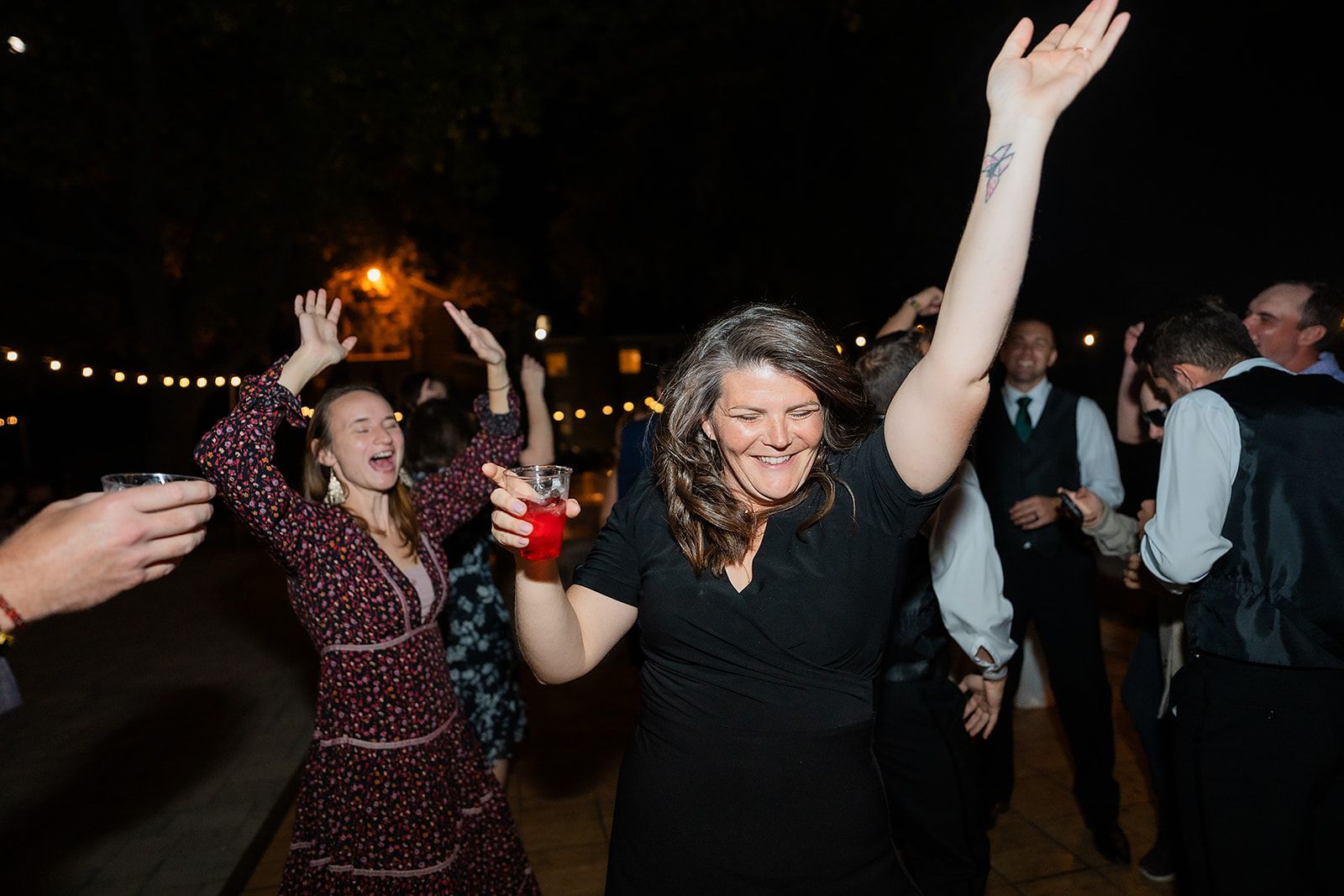 A group of people are dancing at a wedding reception with their arms in the air.