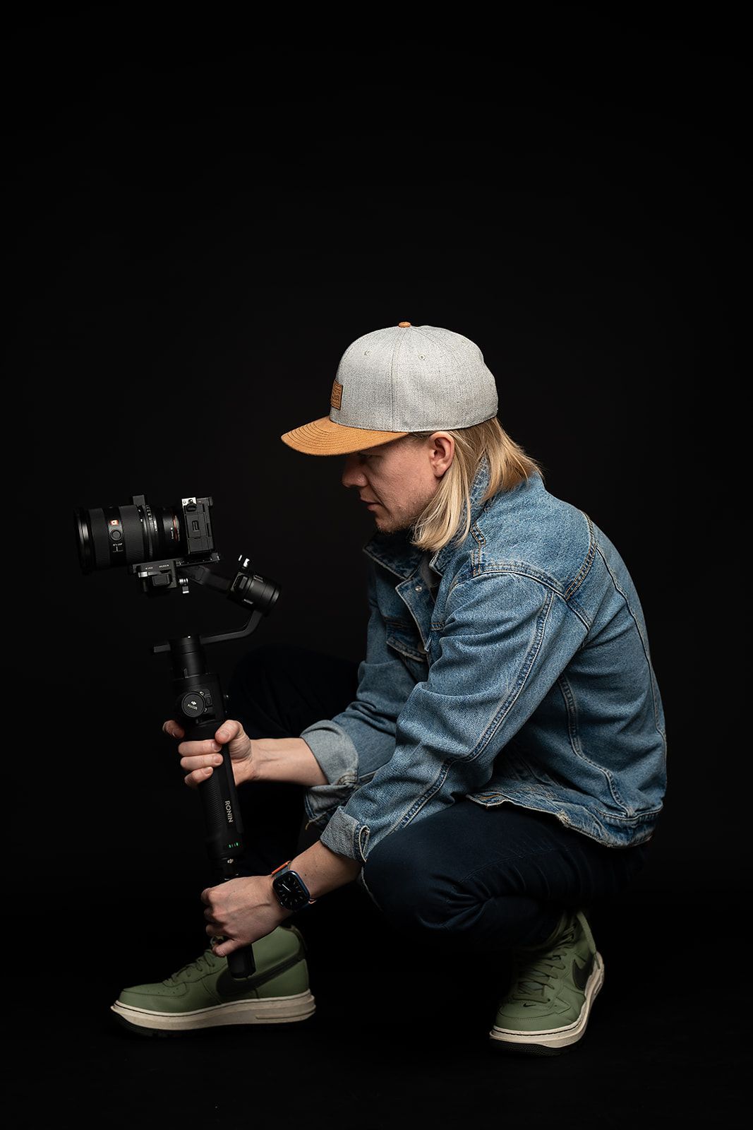 A man is kneeling down while holding a camera on a gimbal.