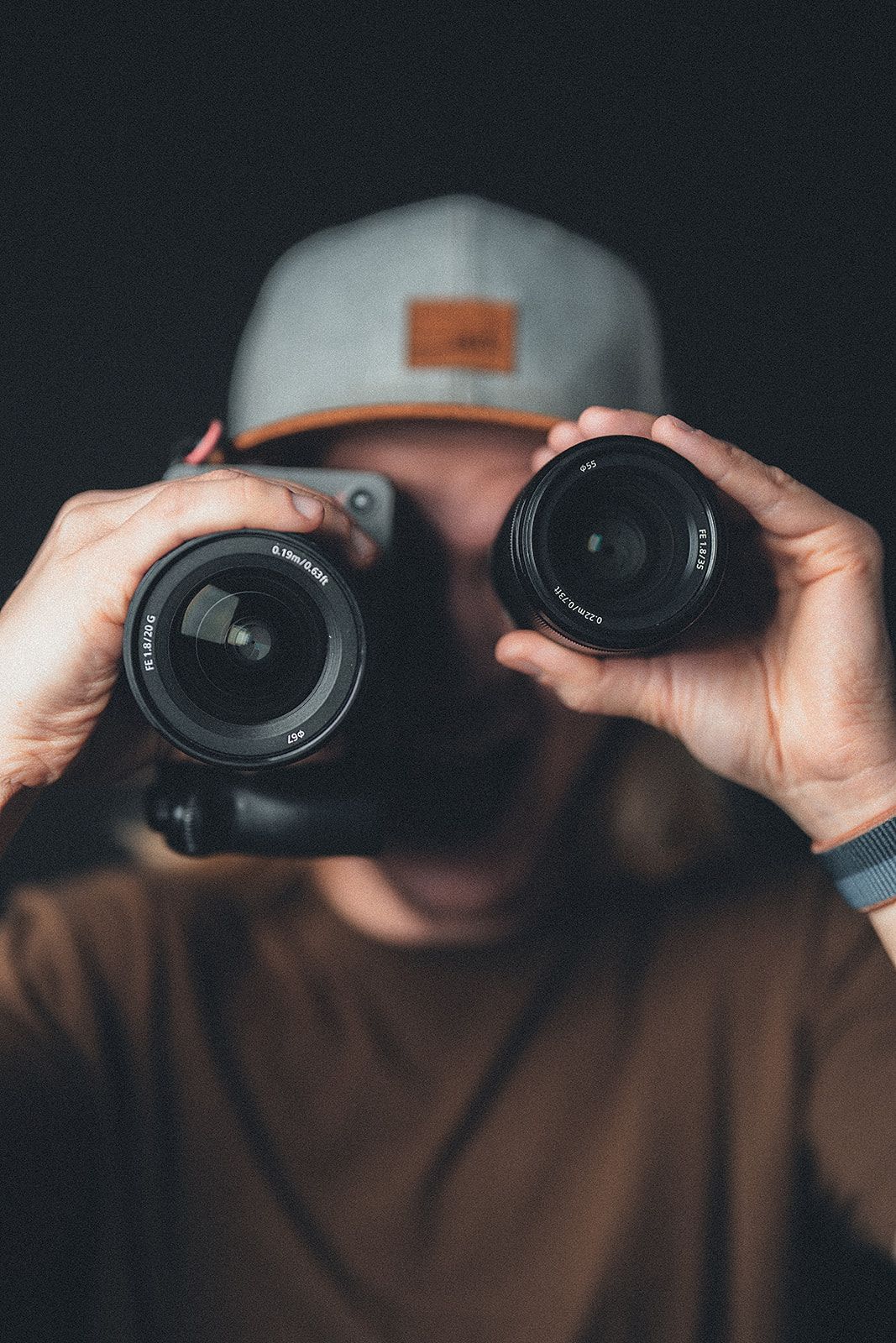 A man is holding two camera lenses in front of his face.