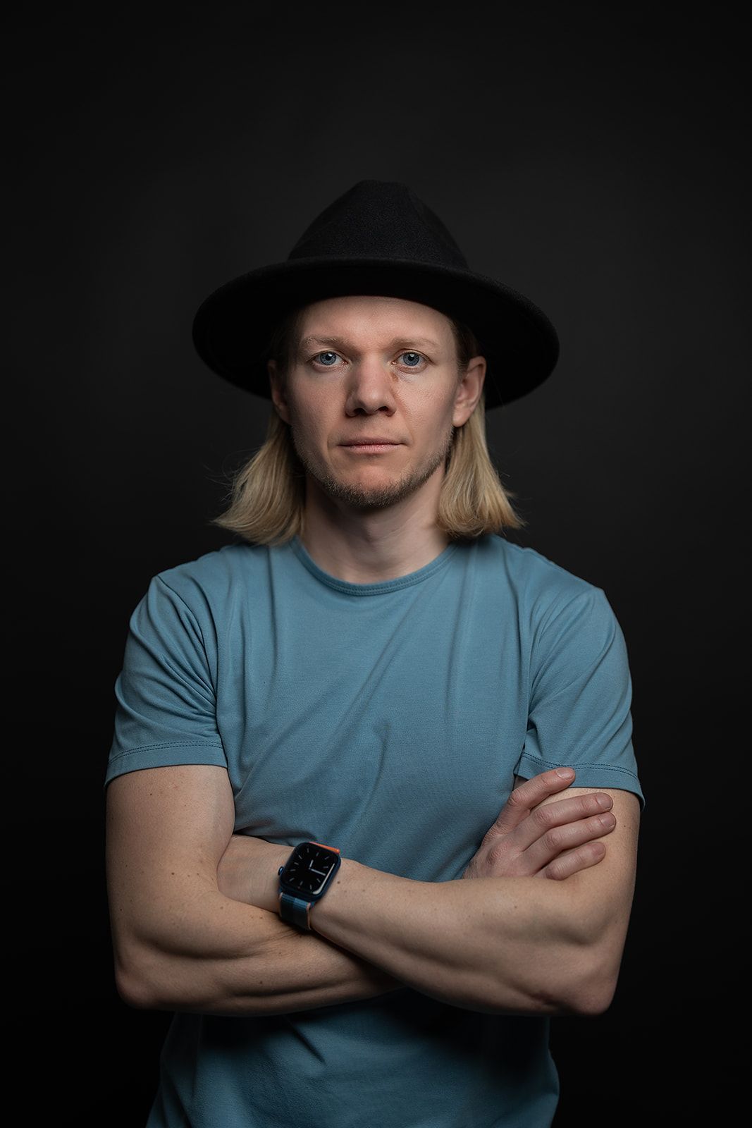A man wearing a hat and a watch is standing with his arms crossed.