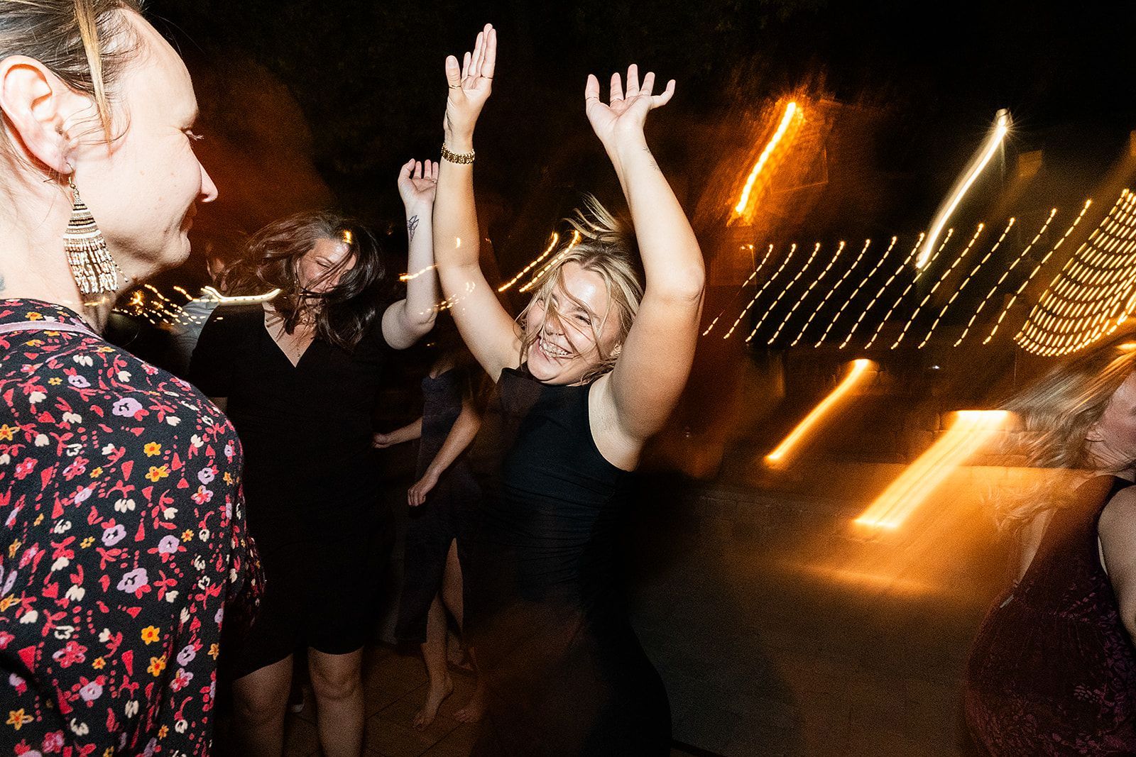 A group of people are dancing at a party with their arms in the air.