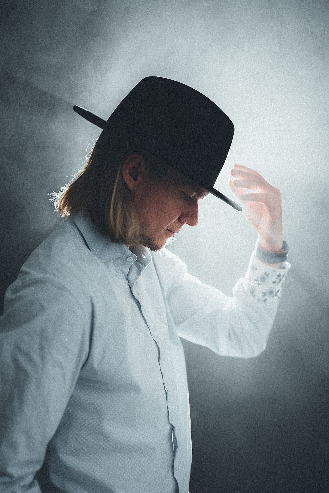 A man wearing a white shirt and a black hat is adjusting his hat.