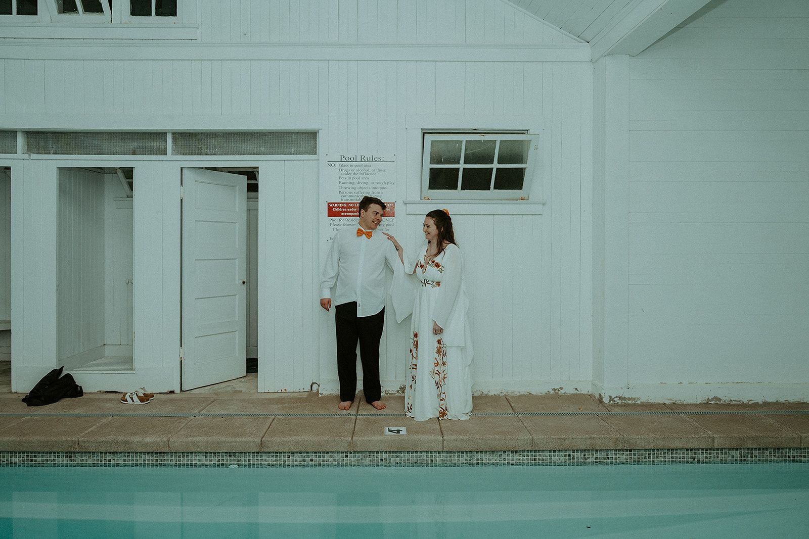 A bride and groom are standing next to a swimming pool.