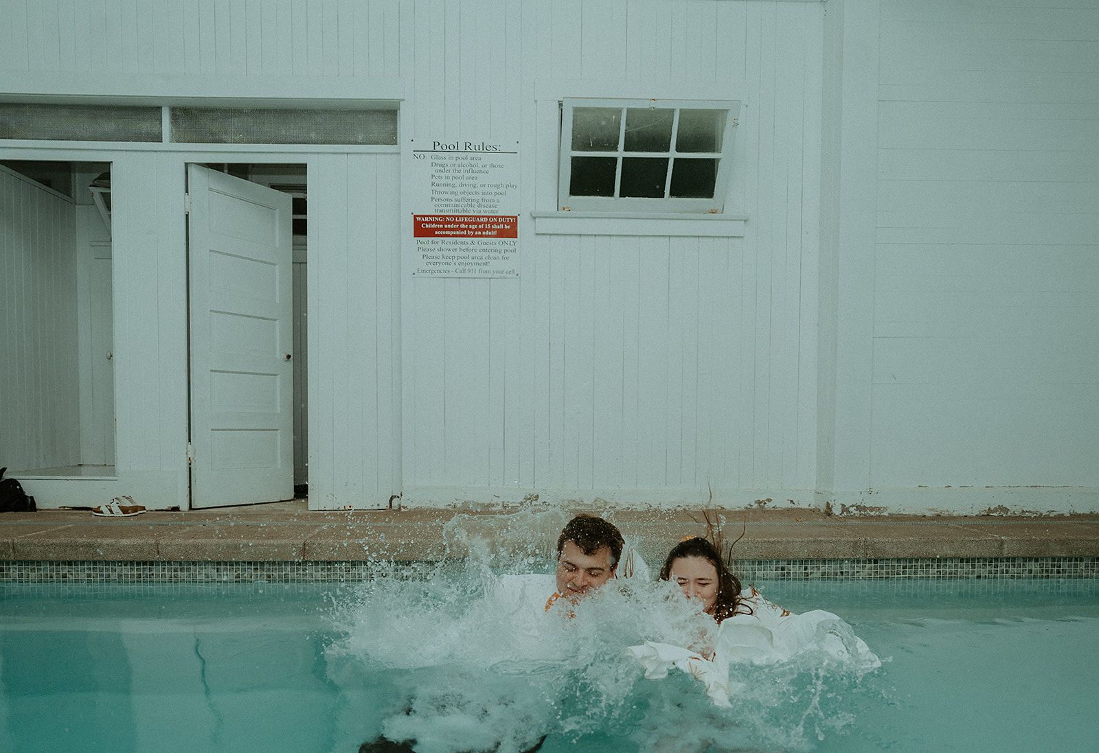 A bride and groom are jumping into a swimming pool.