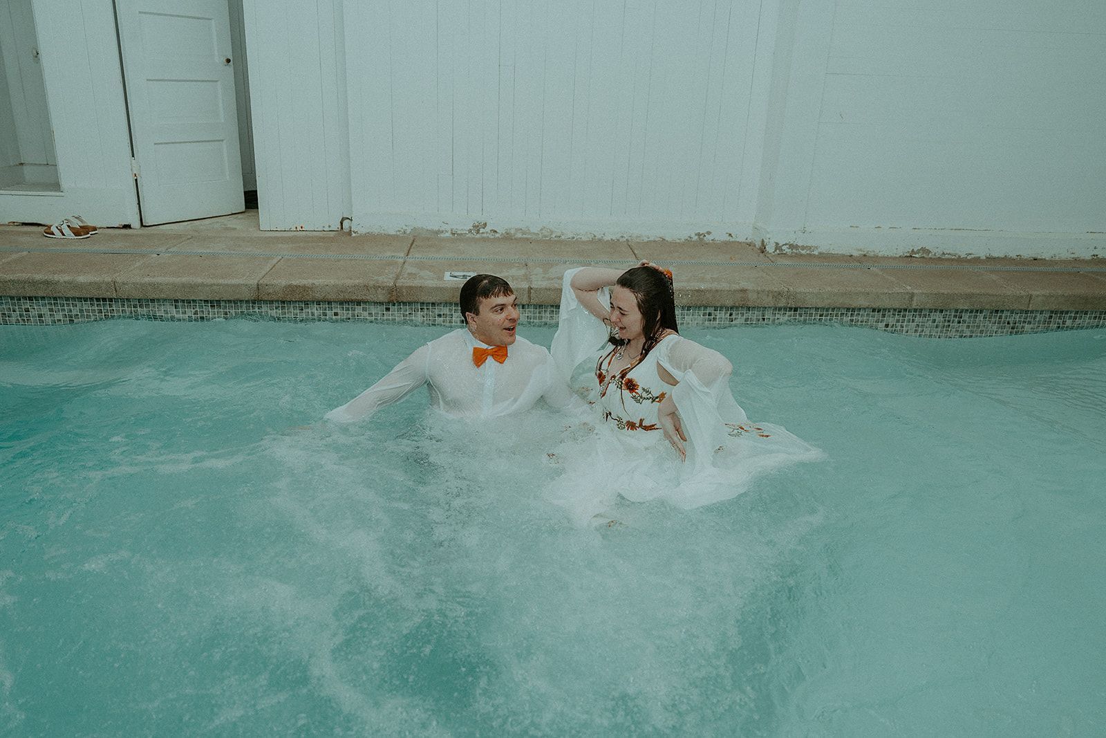 A bride and groom are playing in a swimming pool.