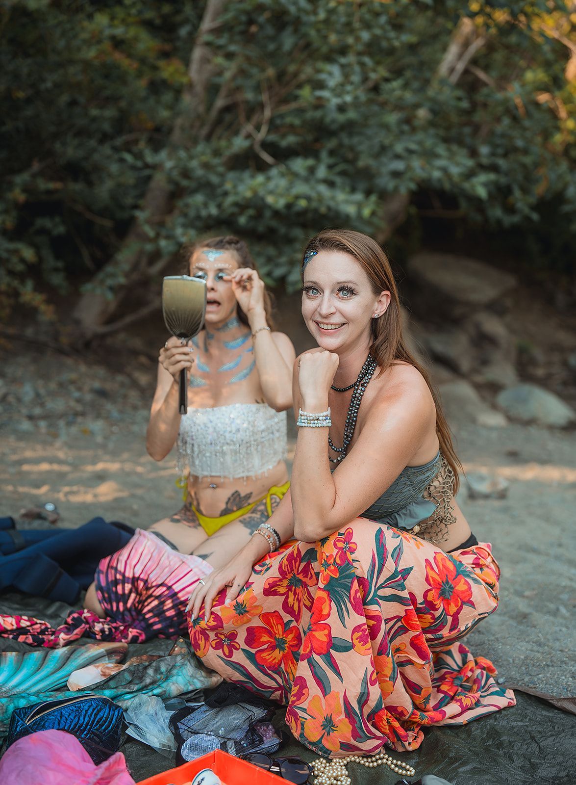 Two women are sitting on the ground looking at themselves in a mirror.