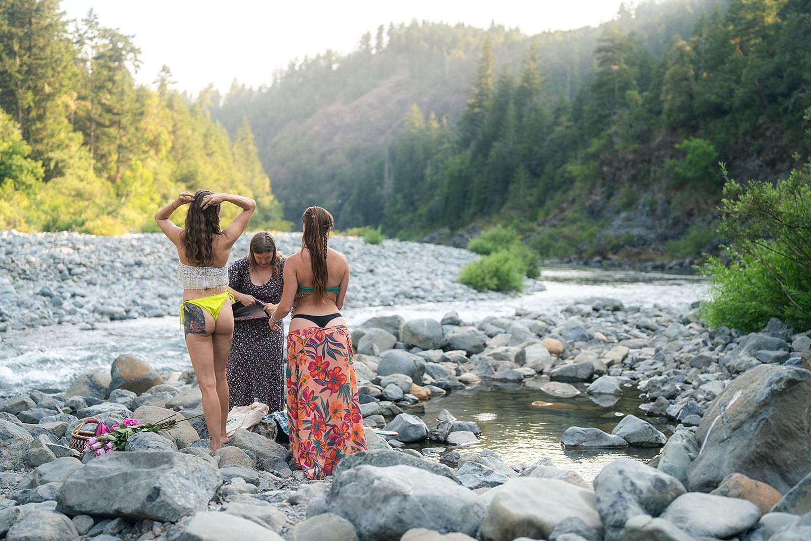 Three women are standing on rocks next to a river.