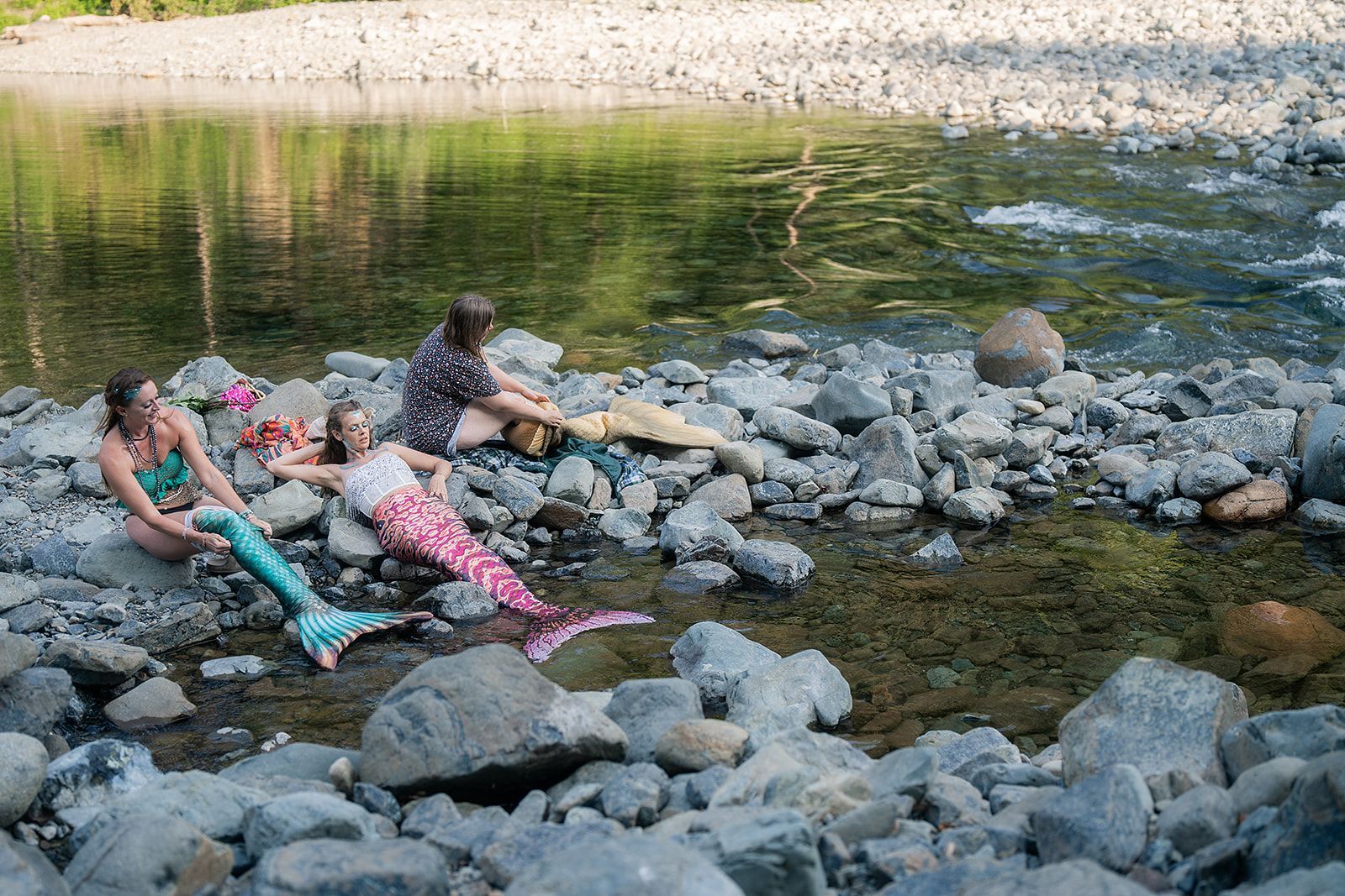 A group of mermaids are sitting on the rocks near a river.