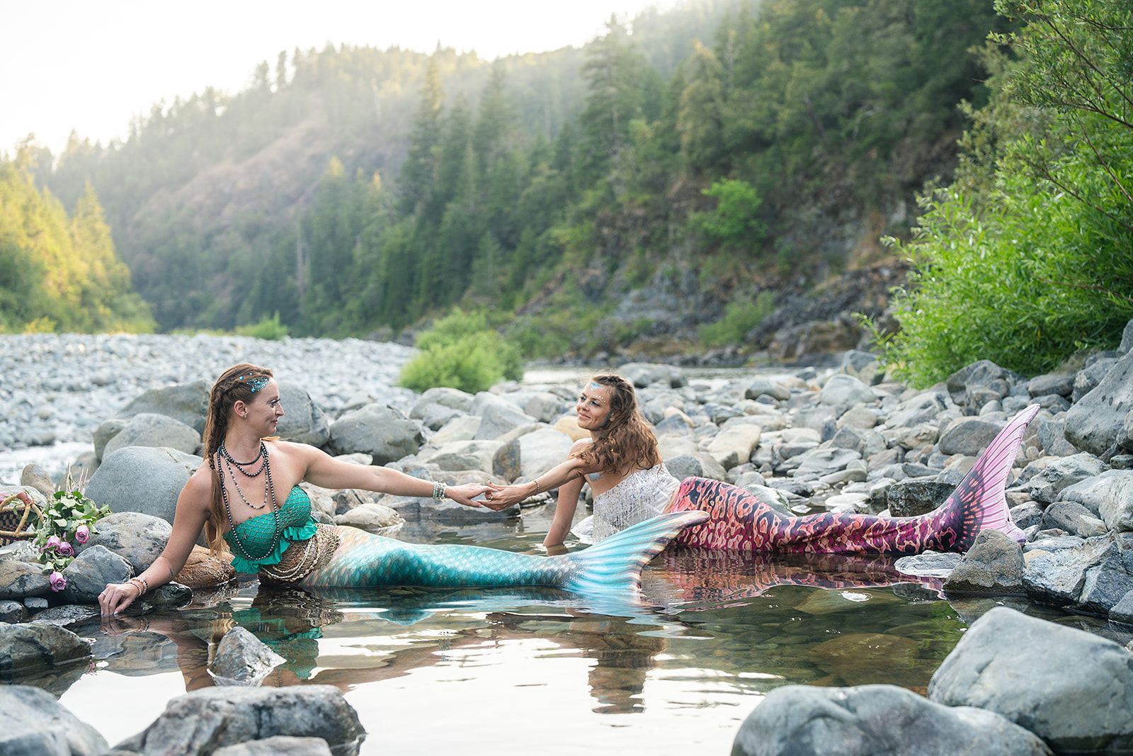 Two mermaids are holding hands in a river.