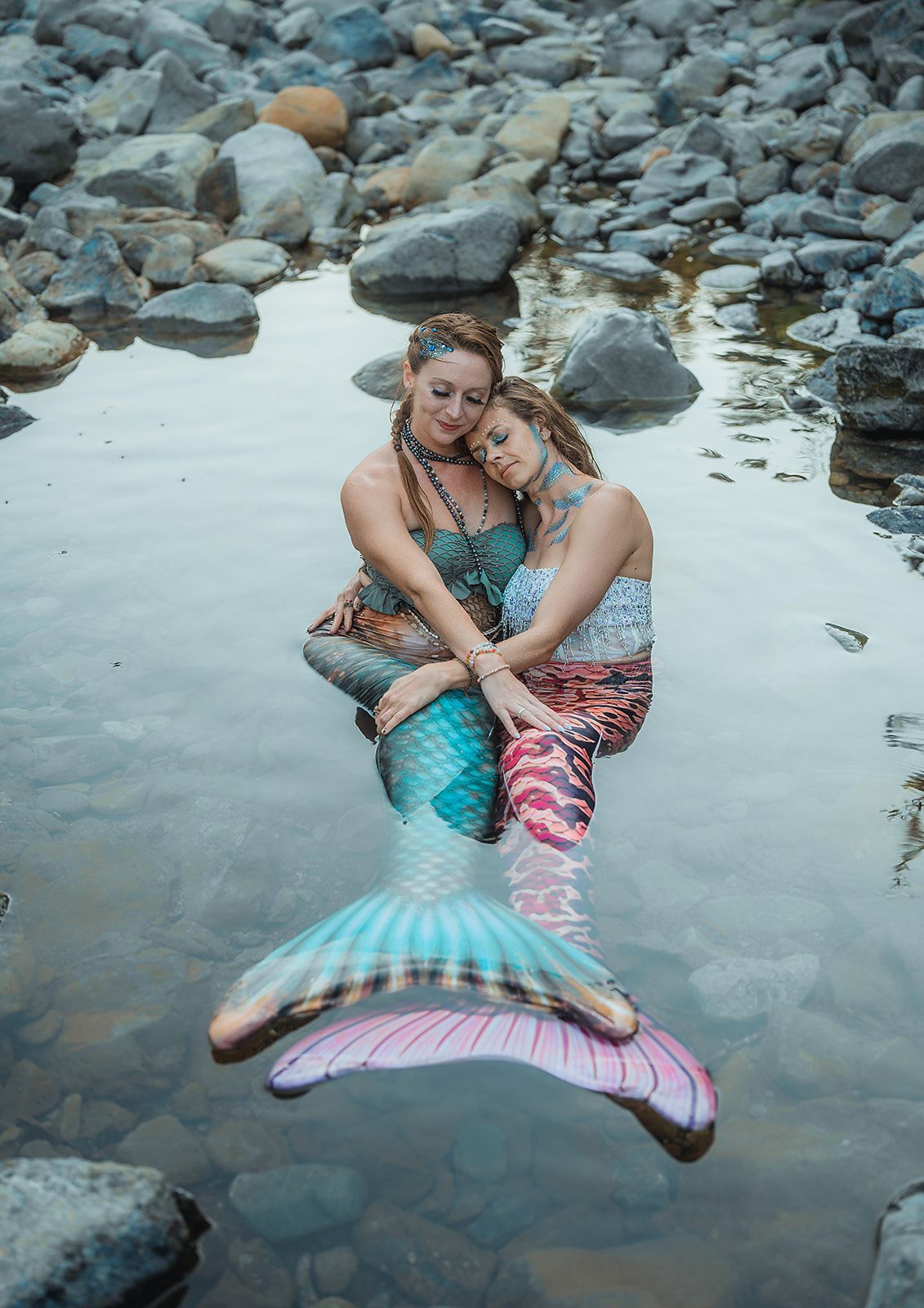 Two mermaids are hugging each other in the water.