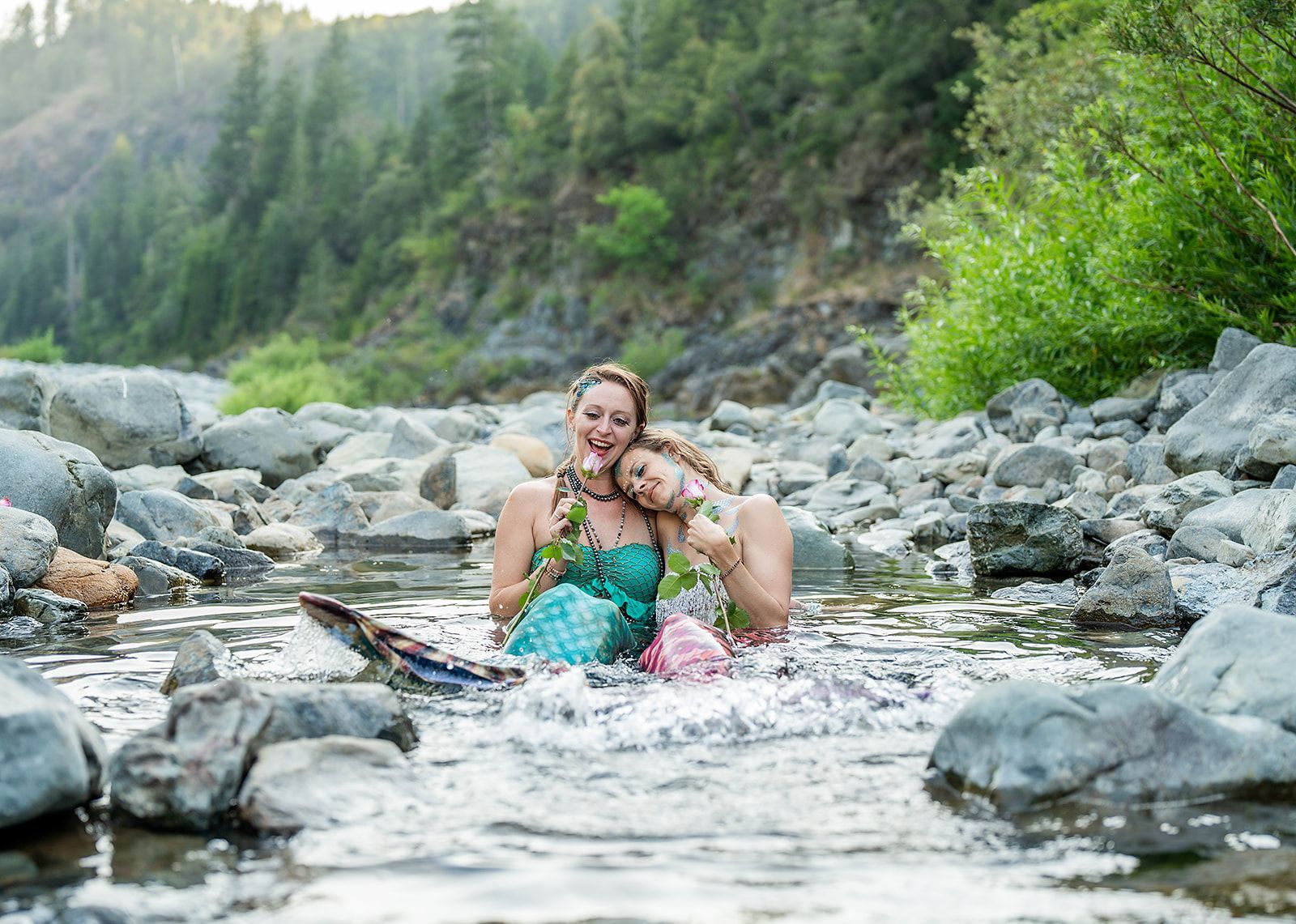 Two mermaids are sitting in a stream of water.