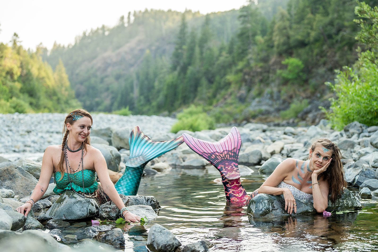 Two mermaids are sitting on rocks in a river.