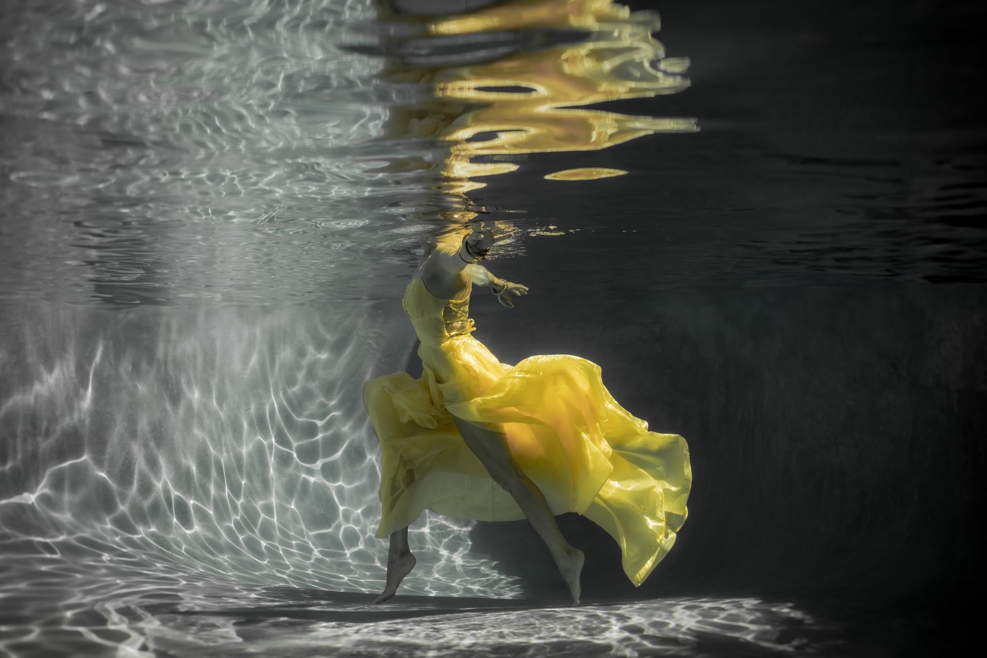 A woman in a yellow dress is swimming underwater.