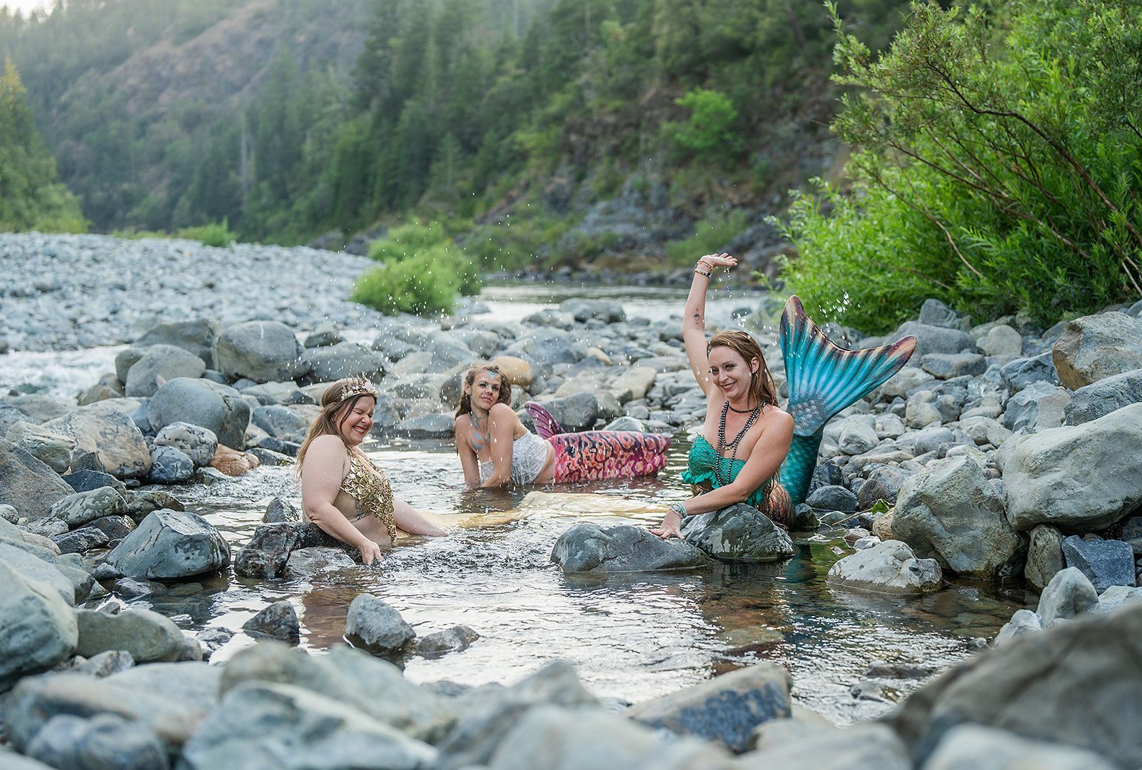Three mermaids are sitting on rocks in a river.