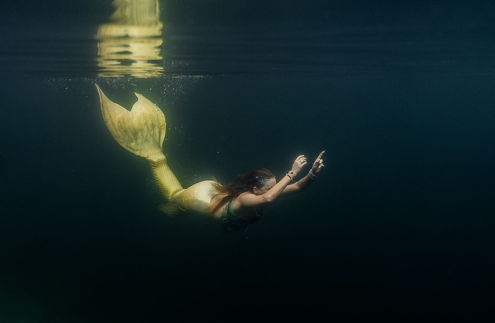 A woman in a mermaid costume is swimming underwater in the ocean.