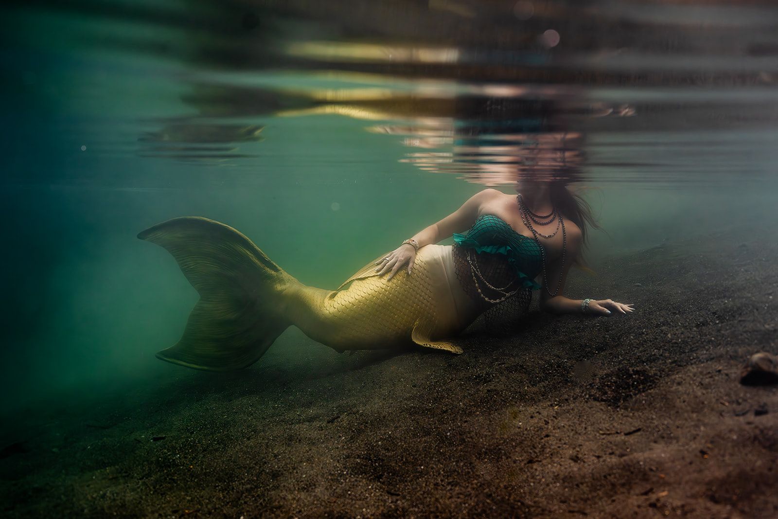 A mermaid is laying on the ground underwater.