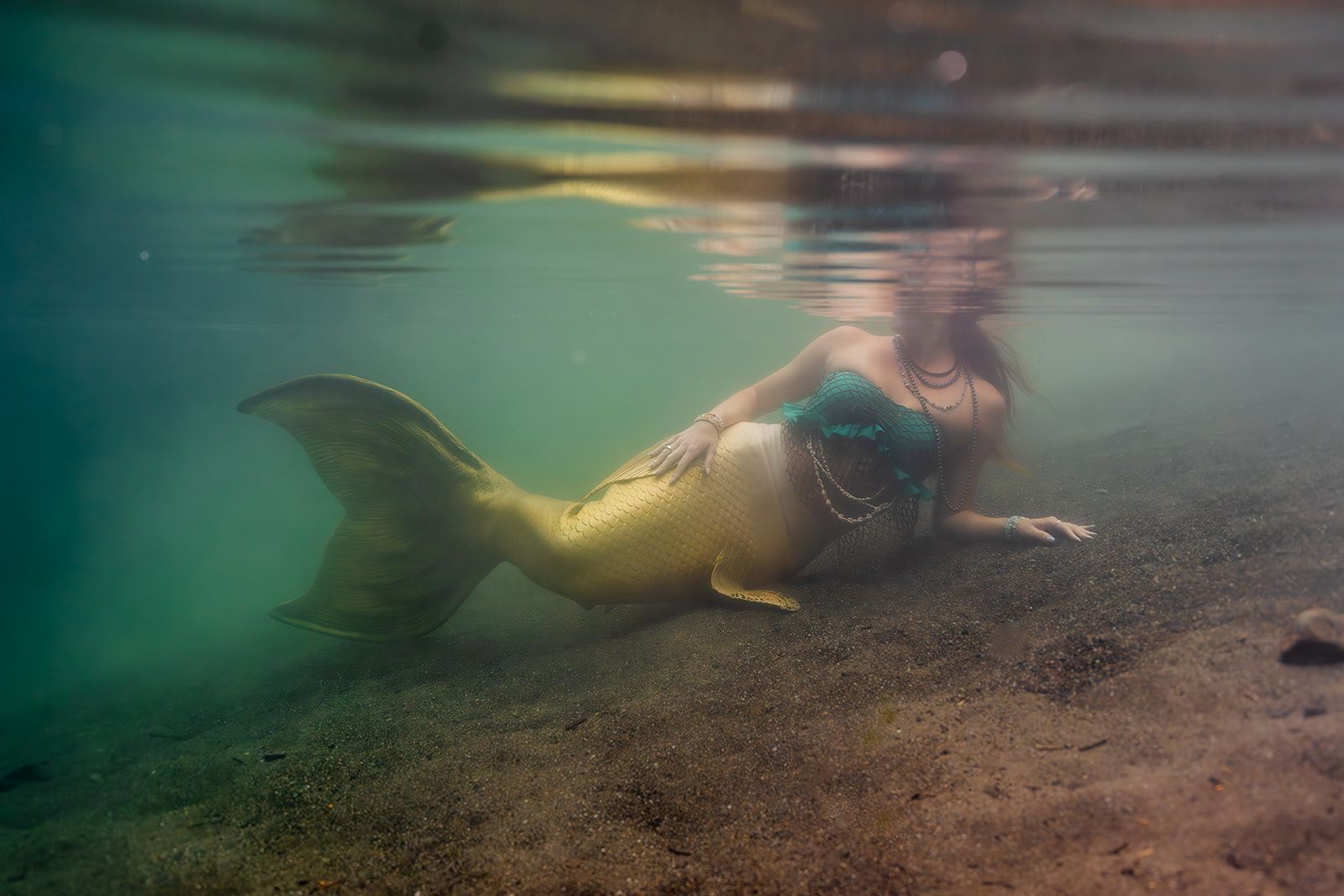 A mermaid is laying on the ground underwater.