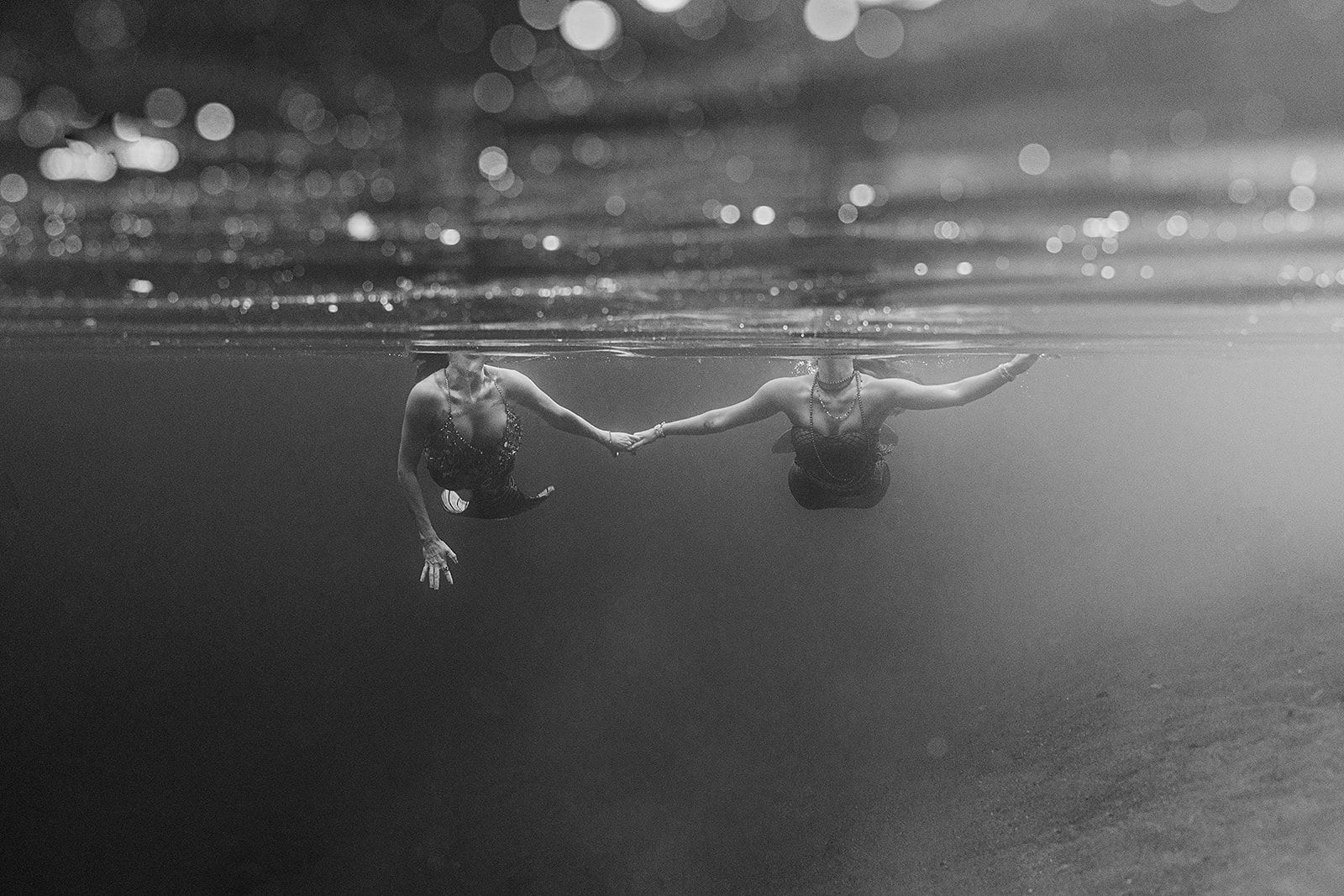 Two people are holding hands underwater in a black and white photo.