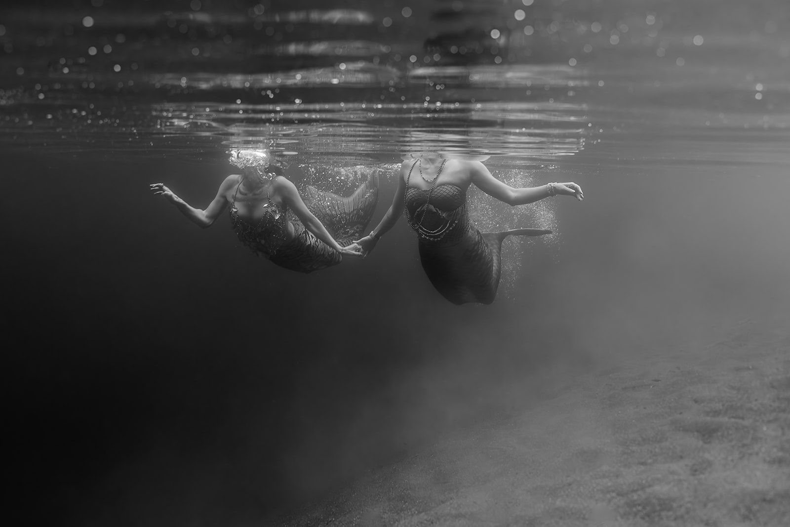Two women are swimming underwater in a black and white photo.