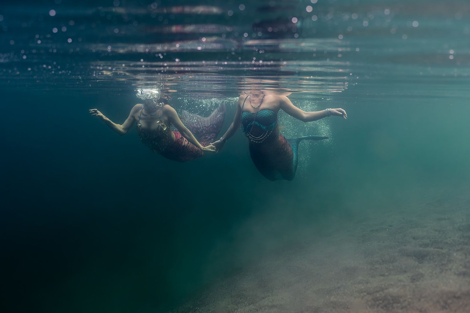 Two mermaids are swimming underwater in the ocean.