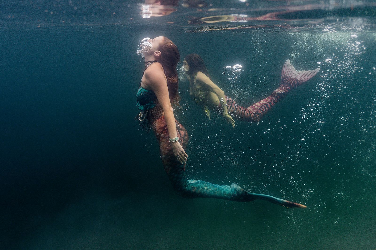 Two mermaids are swimming underwater in the ocean.