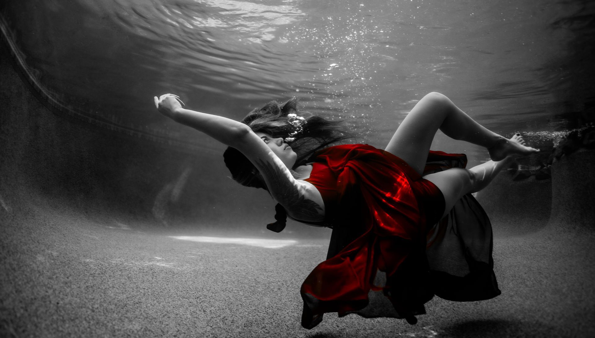 A woman in a red dress is swimming underwater in a pool.
