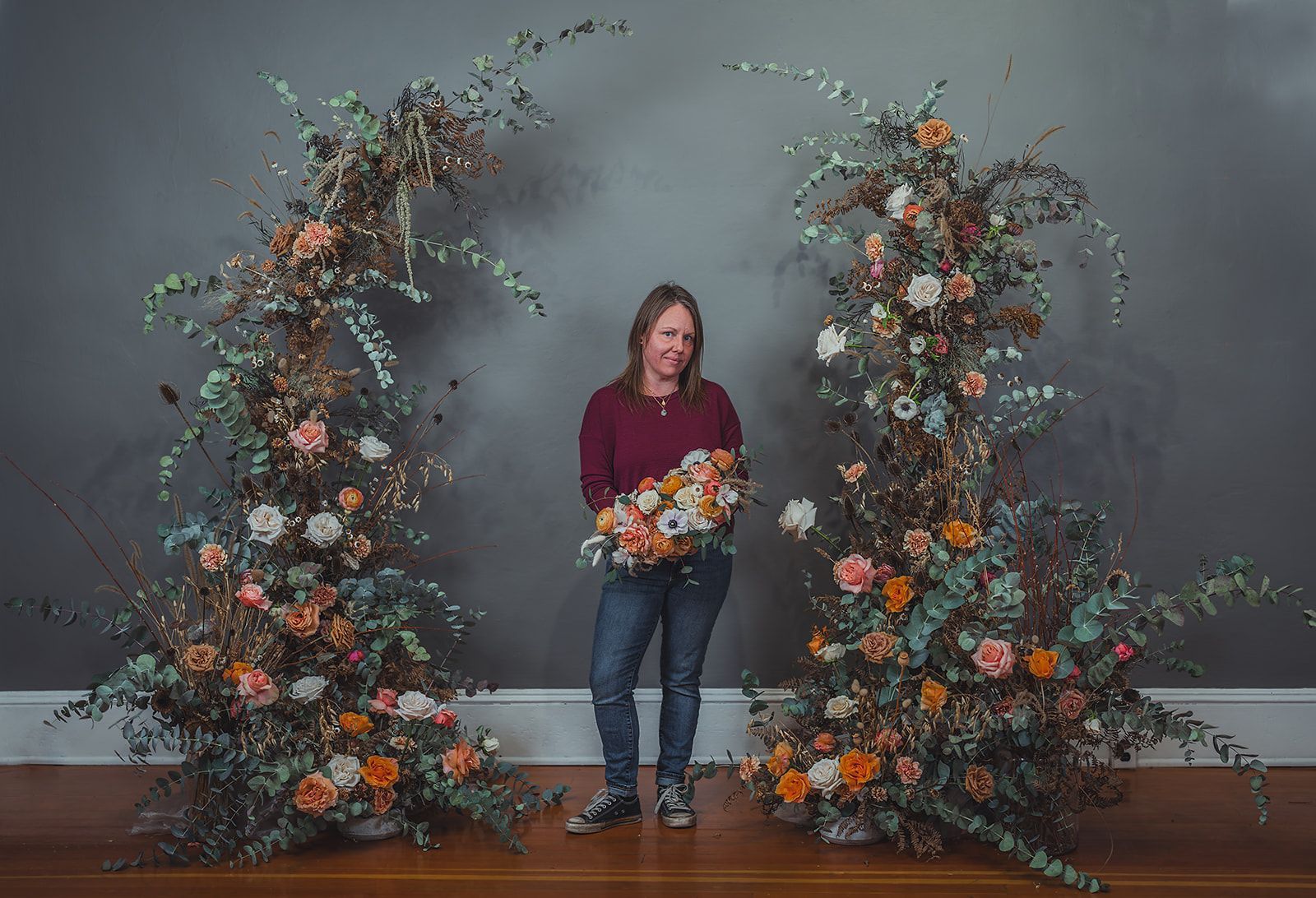 A woman is standing in front of a large floral arrangement.