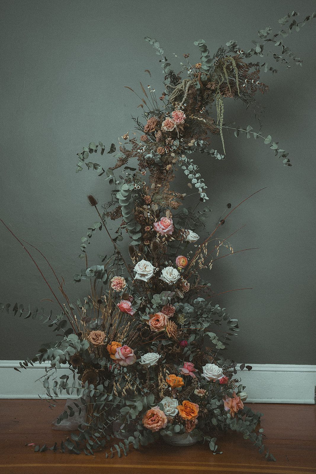 A large bouquet of flowers is sitting on a wooden floor in front of a wall.
